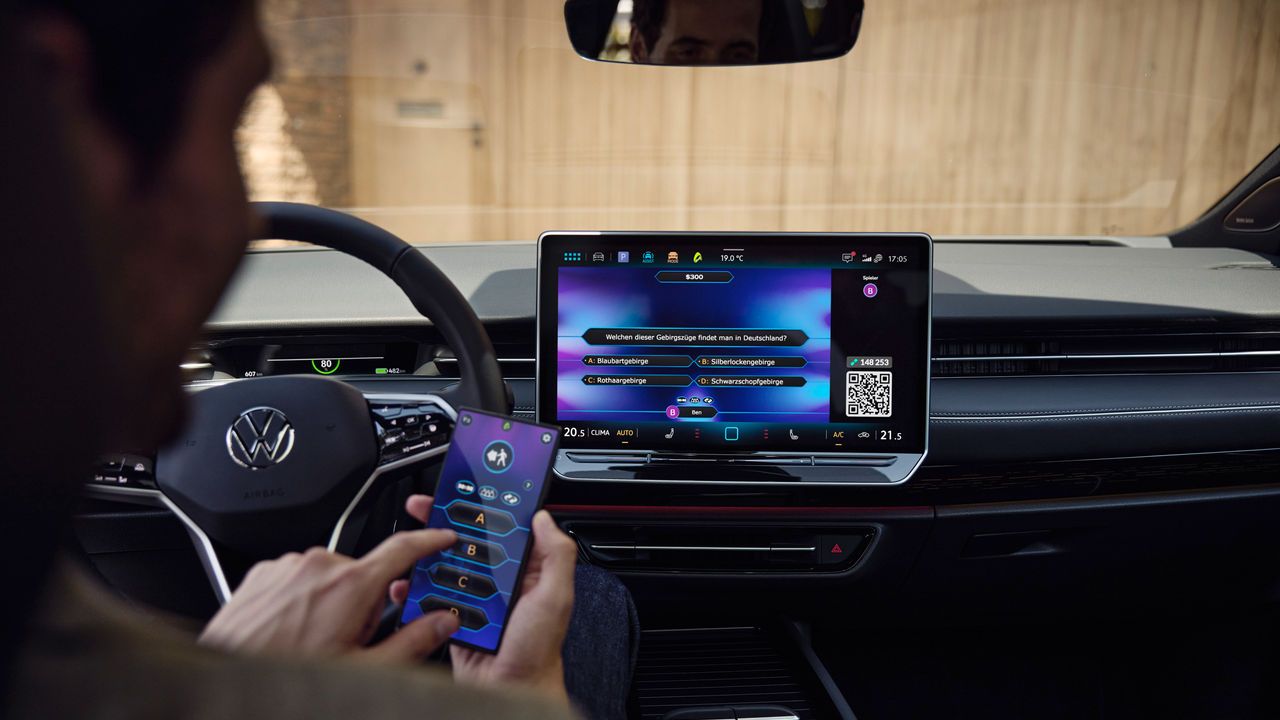 Ein Mann spielt im VW ID.7 Tourer per In-Car-App ein Quiz am Smartphone.