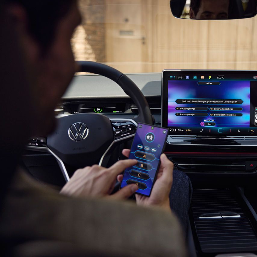 Ein Mann spielt im VW ID.7 Tourer per In-Car-App ein Quiz am Smartphone.
