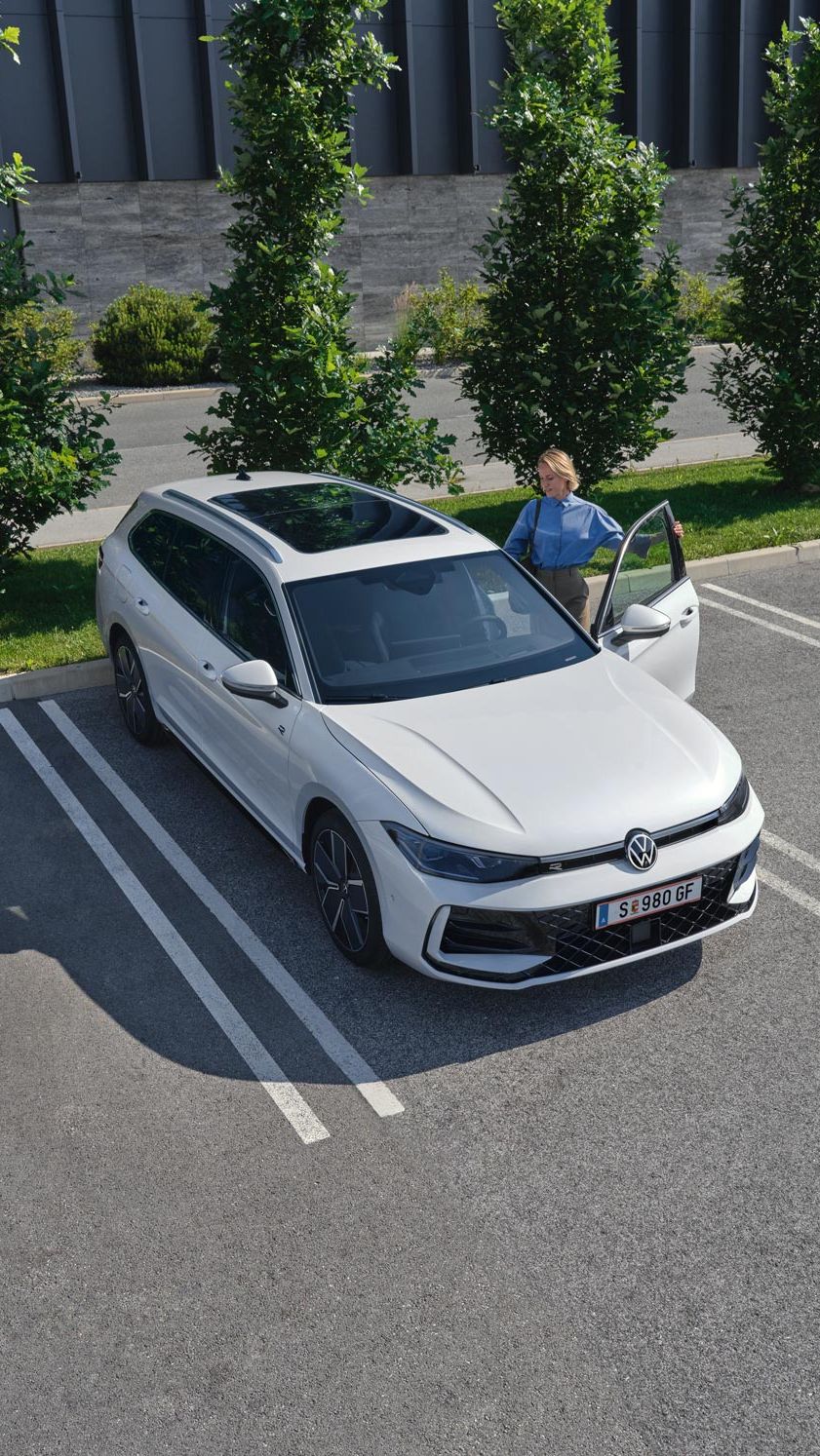 Weißer VW Passat parkt vor einem modernen Bürogebäude. Eine Frau steigt ein.