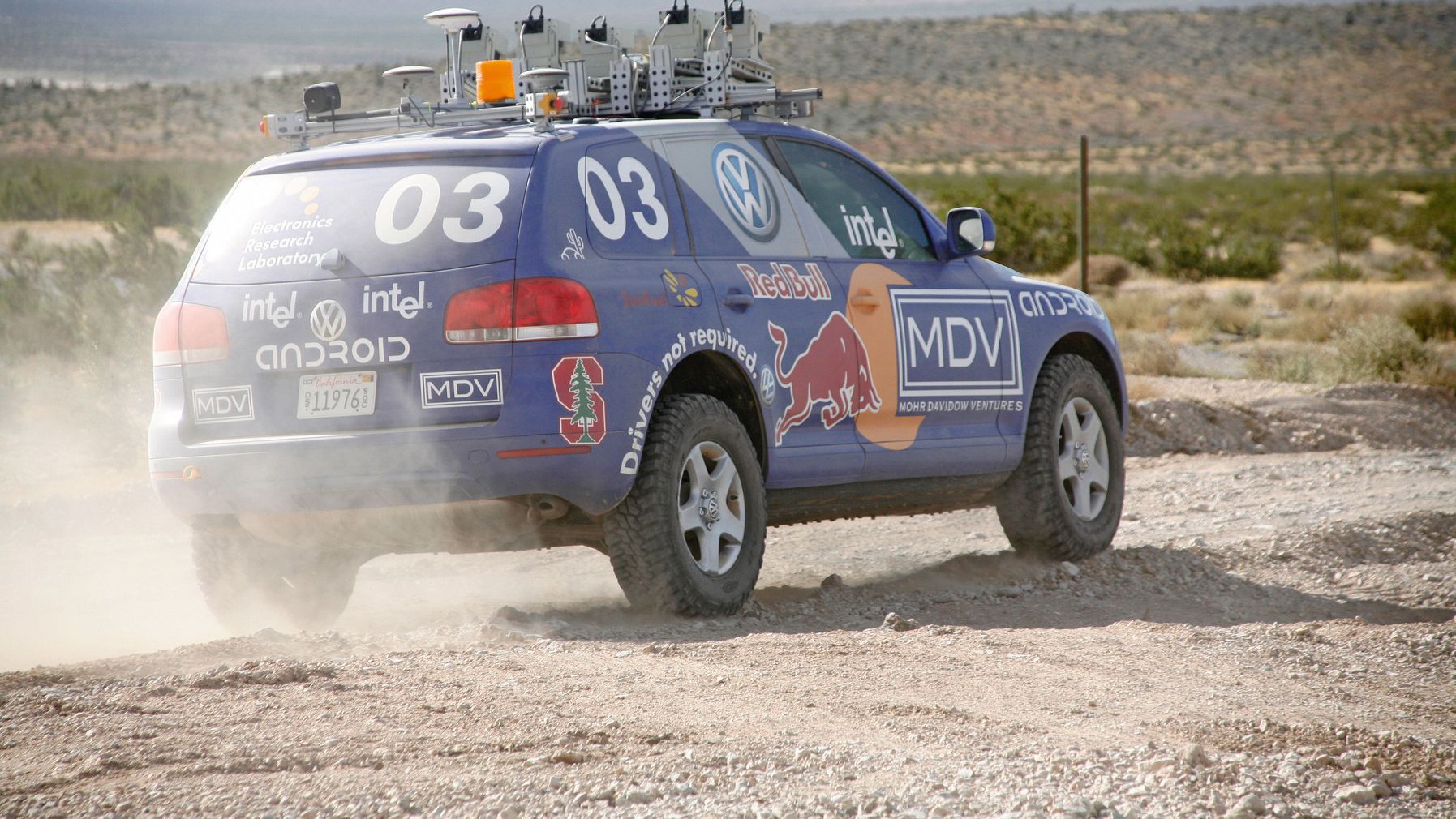Ein blauer Touareg mit Sponsoren-Beklebung fährt driftet auf einer Schotterstraße