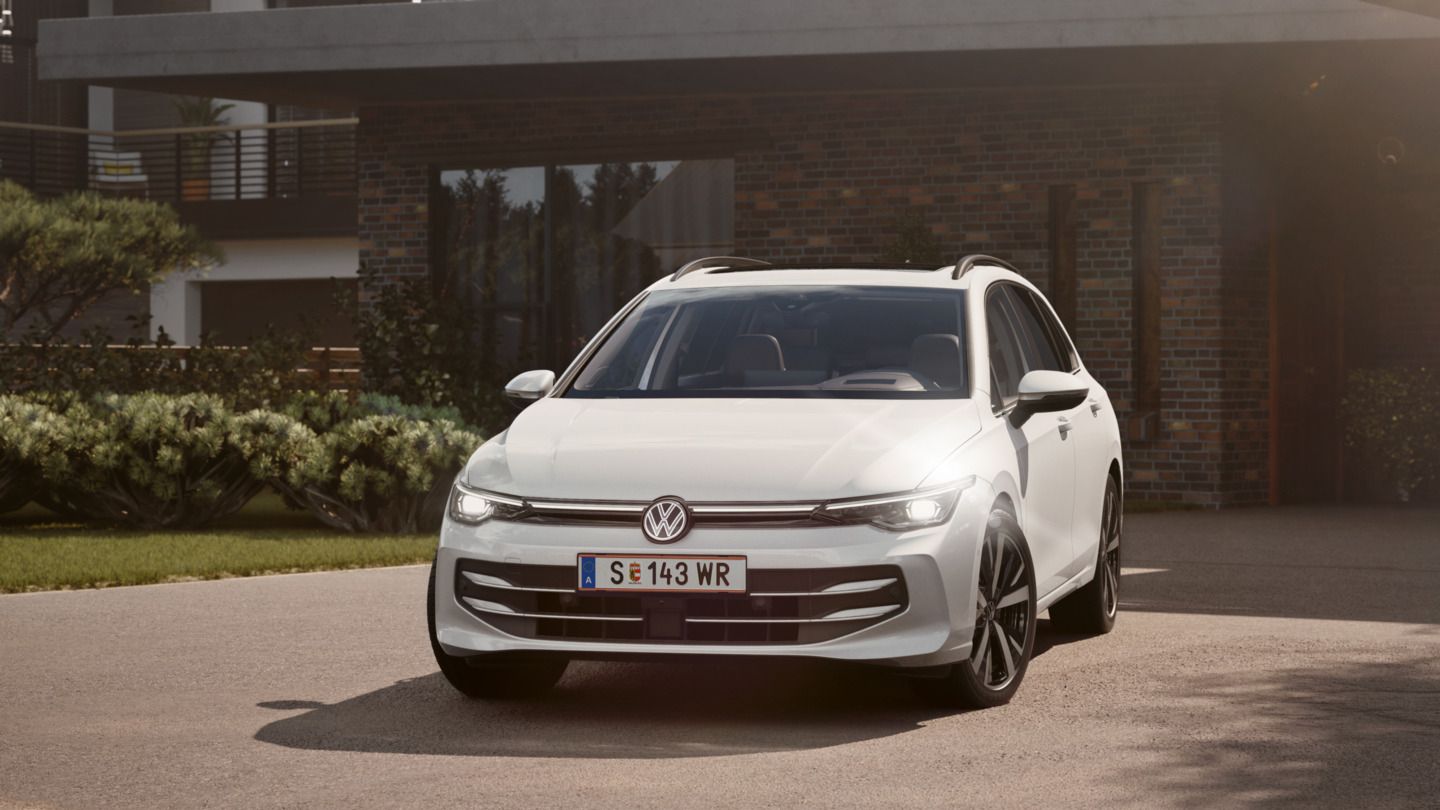 Ein weißer VW Golf Variant parkt in der Auffahrt eines Bungalows mit aktivem Tagfahrlicht.