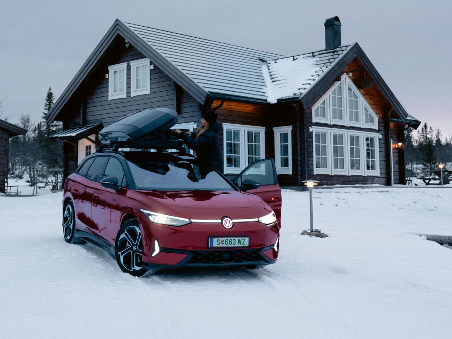 Ein roter ID.7 Tourer GTX mit Dachbox steht im Schnee vor einem Wohnhaus. 