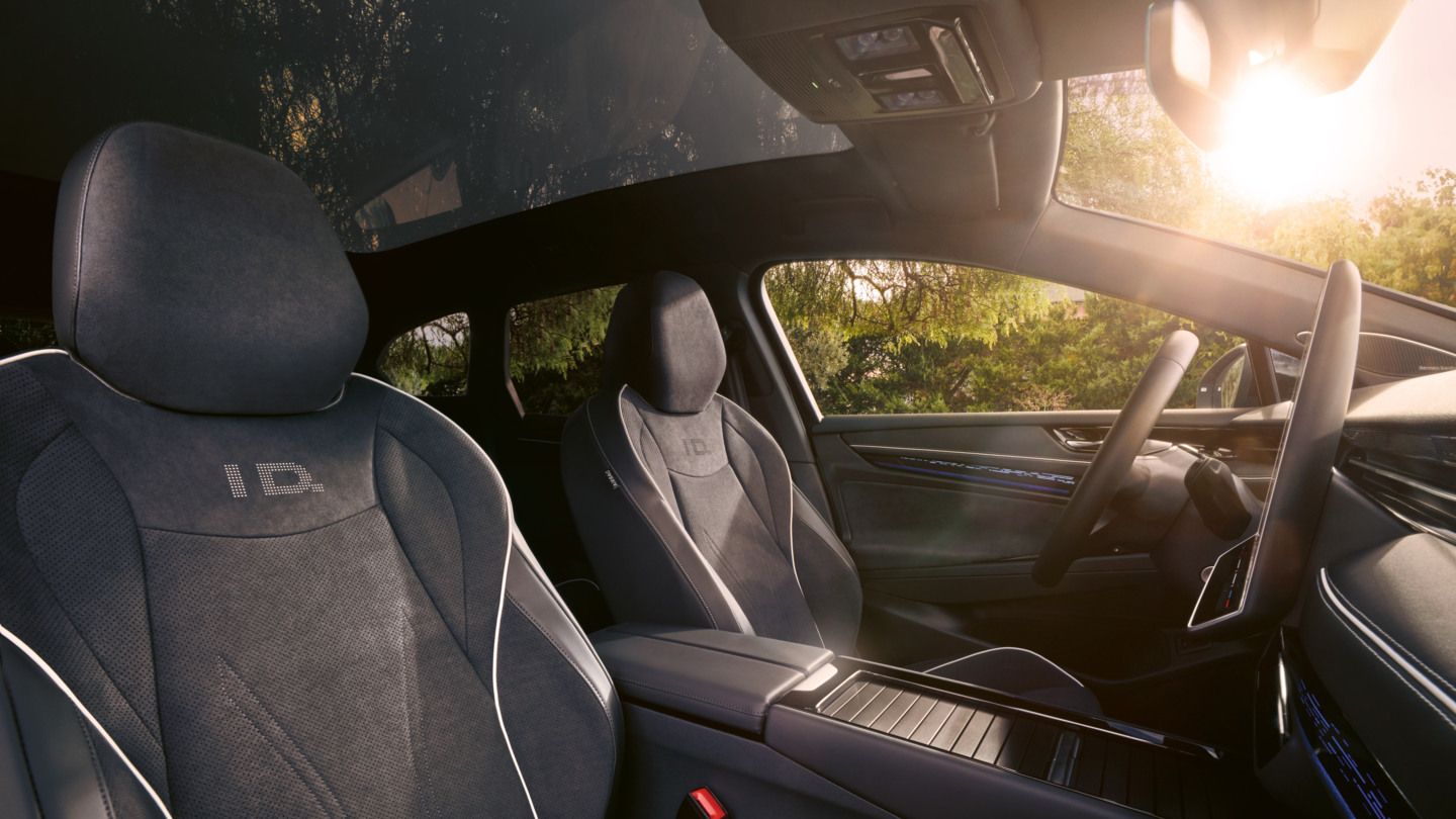 Vordersitze des ID.7 Tourer, Interieur mit Ambientebeleuchtung und Panoramadach. 