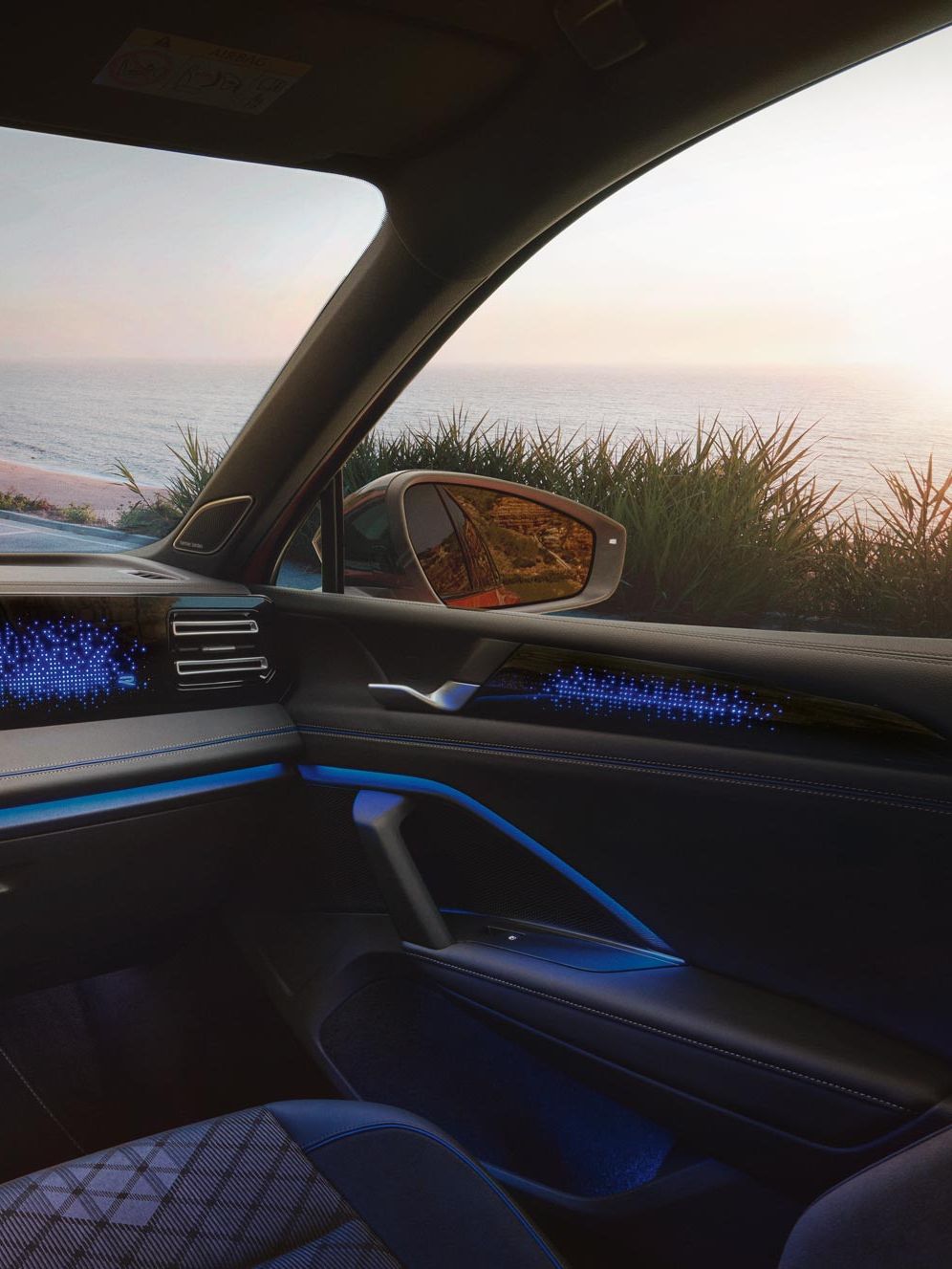 VW Tiguan mit blauer Ambientebeleuchtung. Durch die Frontscheibe ist ein Küstenlandschaft und ein auf das Meer schauendes Paar sichtbar.