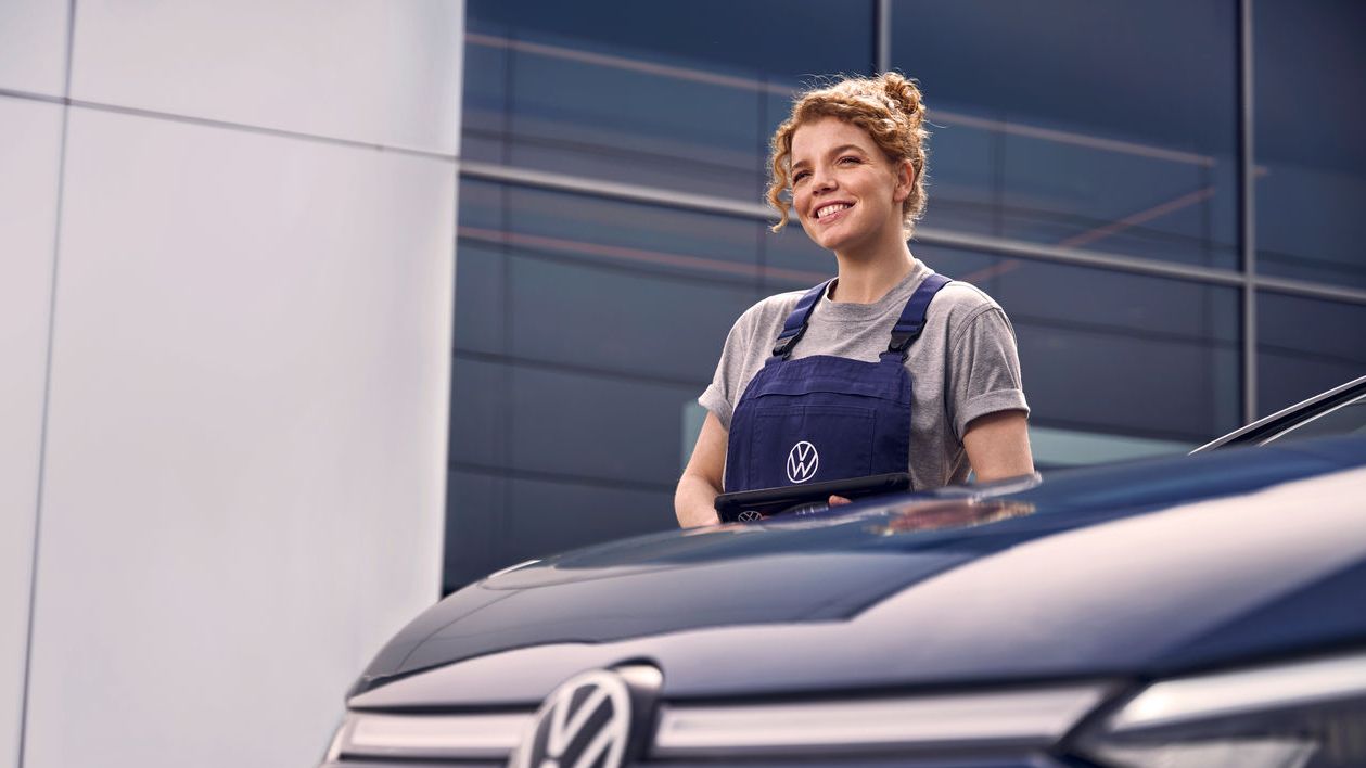 Eine Volkswagen Technikerin vor einer Volkswagen Werkstatt.