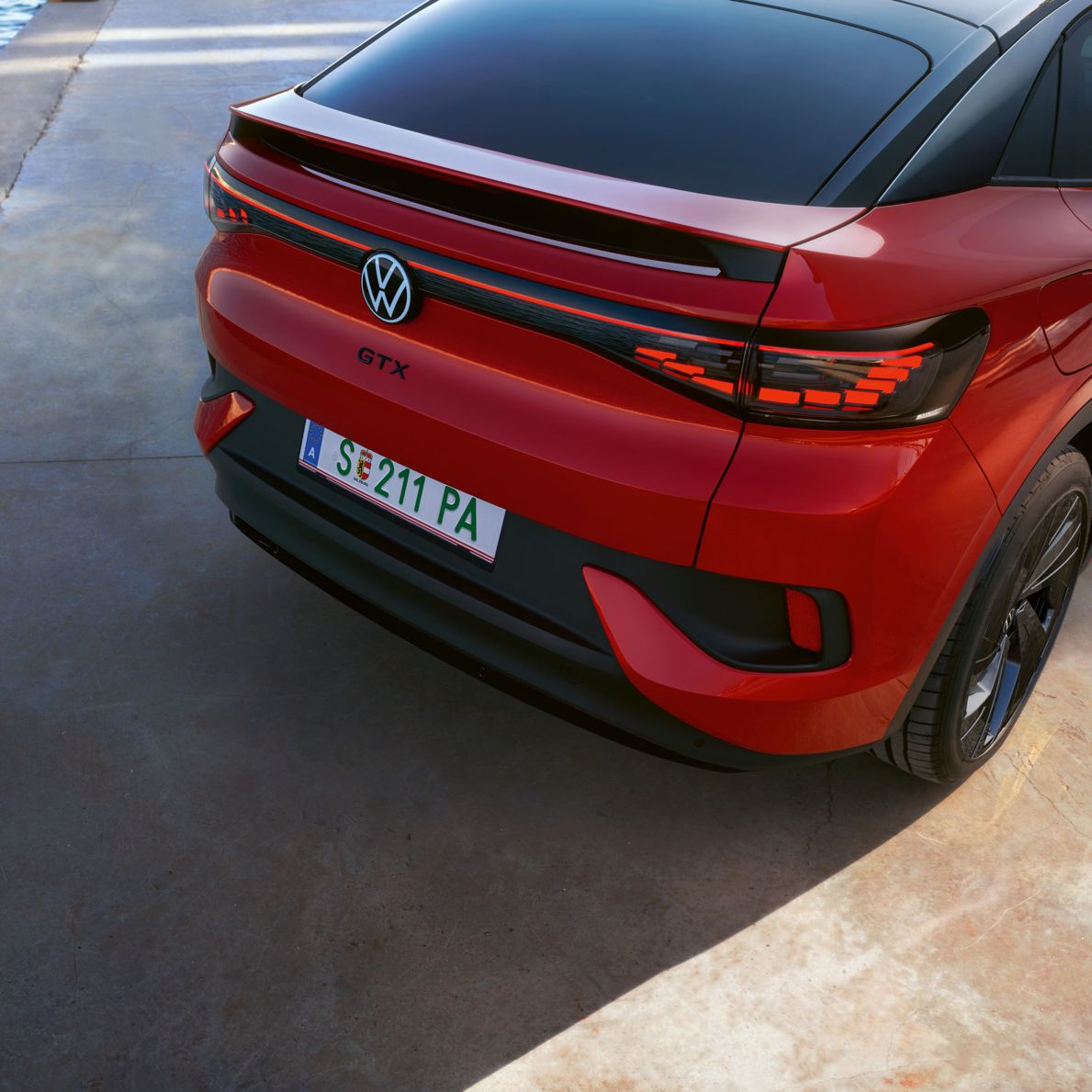 Ein rotes Volkswagen Elektroauto, Modell GTX, steht auf einer betonierten Fläche neben Wasser. Das Auto hat eine italienische Nummernschild und moderne Lichtleisten am Heck.