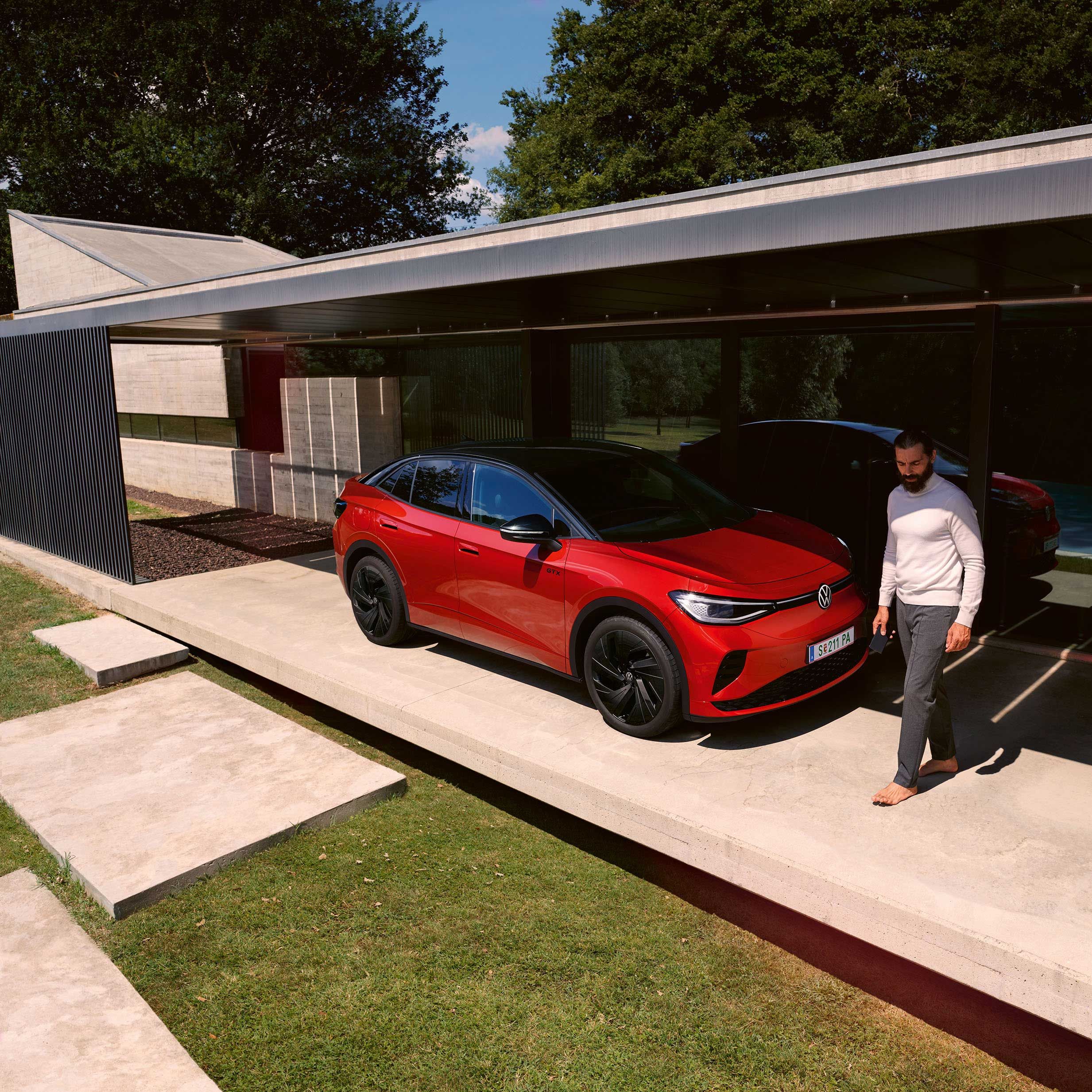Roter VW ID.5 GTX von schräg vorne in einem modernen Carport, ein Mann geht vor der Motorhaube entlang