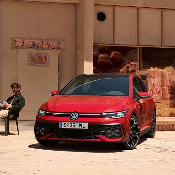 Zwei junge Männer sitzen vor einem Geschäft neben einem roten VW Golf GTI.