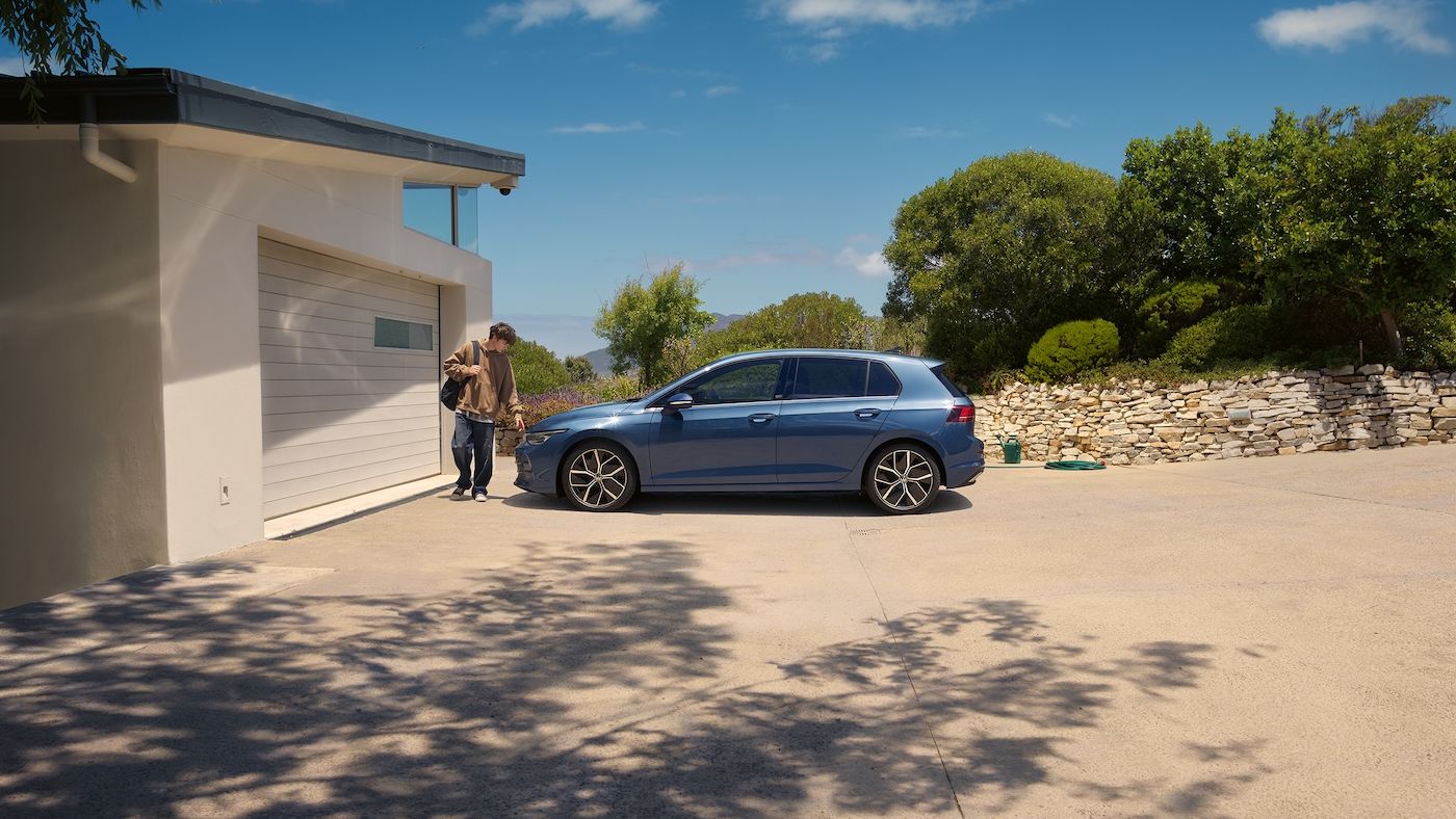 Ein junger Mann geht an einem blauen VW Golf vorbei