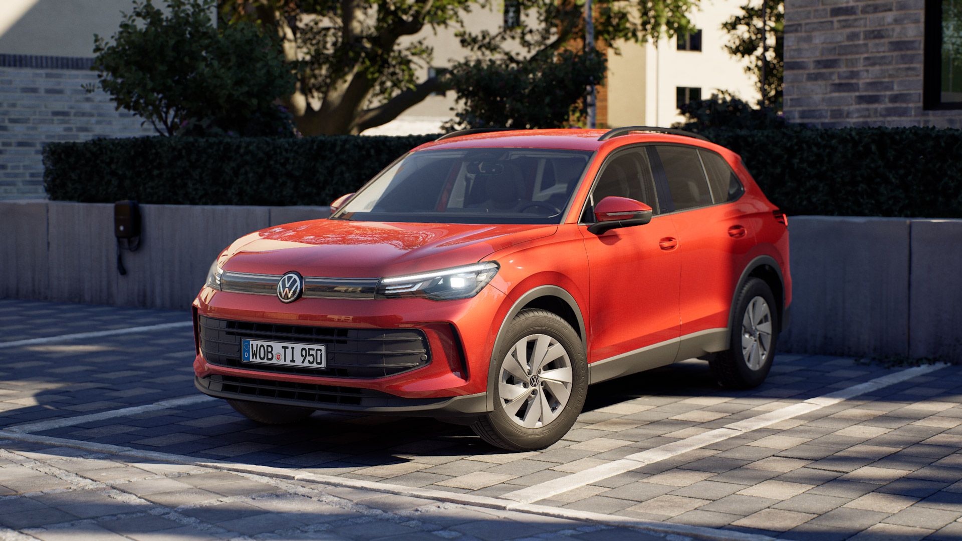 Roter Tiguan von Volkswagen, der auf einem Parkplatz in einer modernen Wohngegend steht. Das Auto ist leicht schräg von vorne fotografiert, sodass Front und Fahrerseite gut sichtbar sind. Im Hintergrund sieht man eine Mauer, Bäume und Wohngebäude aus Klinker.