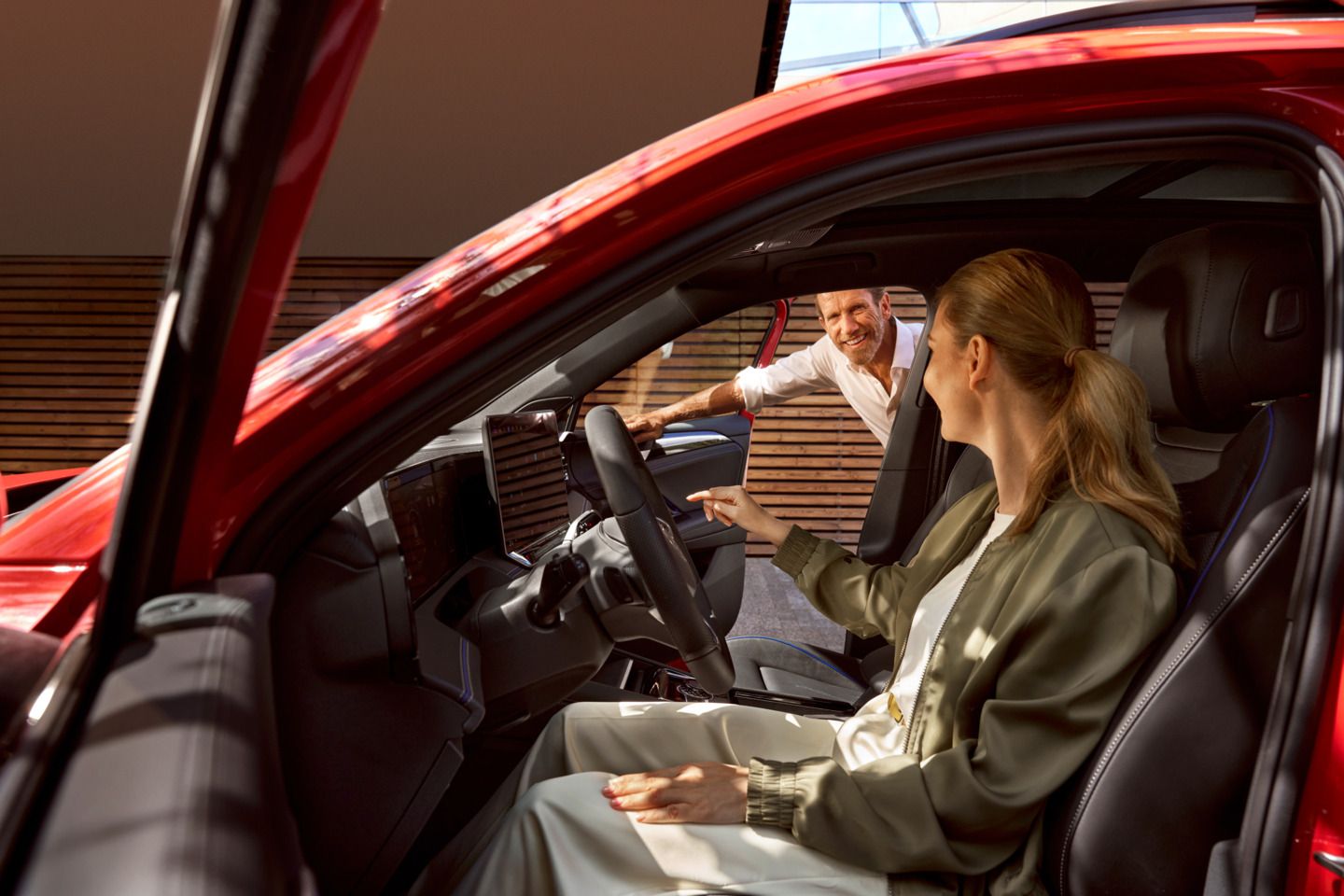 Frau sitzt auf dem Fahrersitz des geparkten Tiguan, während ein Mann durch die offene Beifahrertür schaut