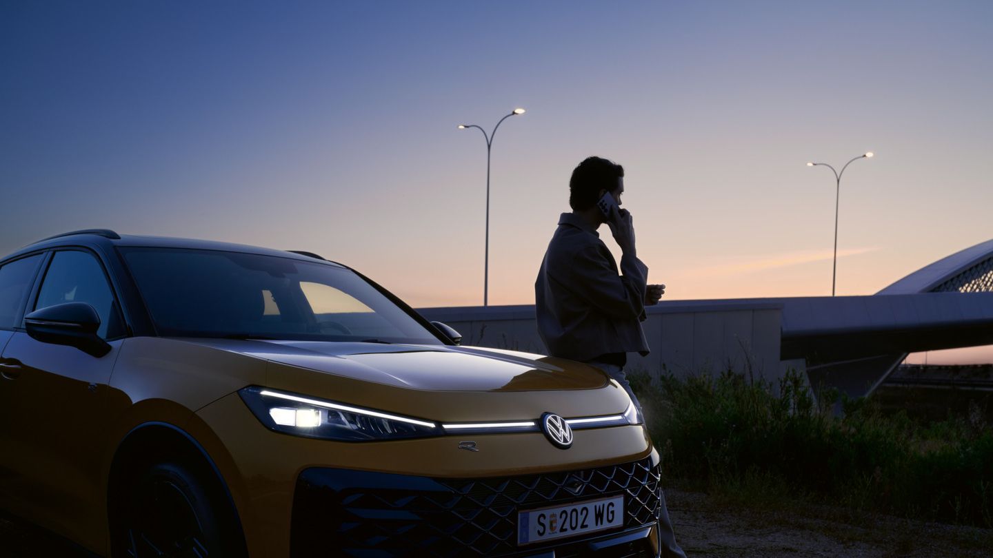 Ein Mann neben einem VW T-Roc R-Line mit eingeschalteten Scheinwerfern und beleuchtetem Logo.