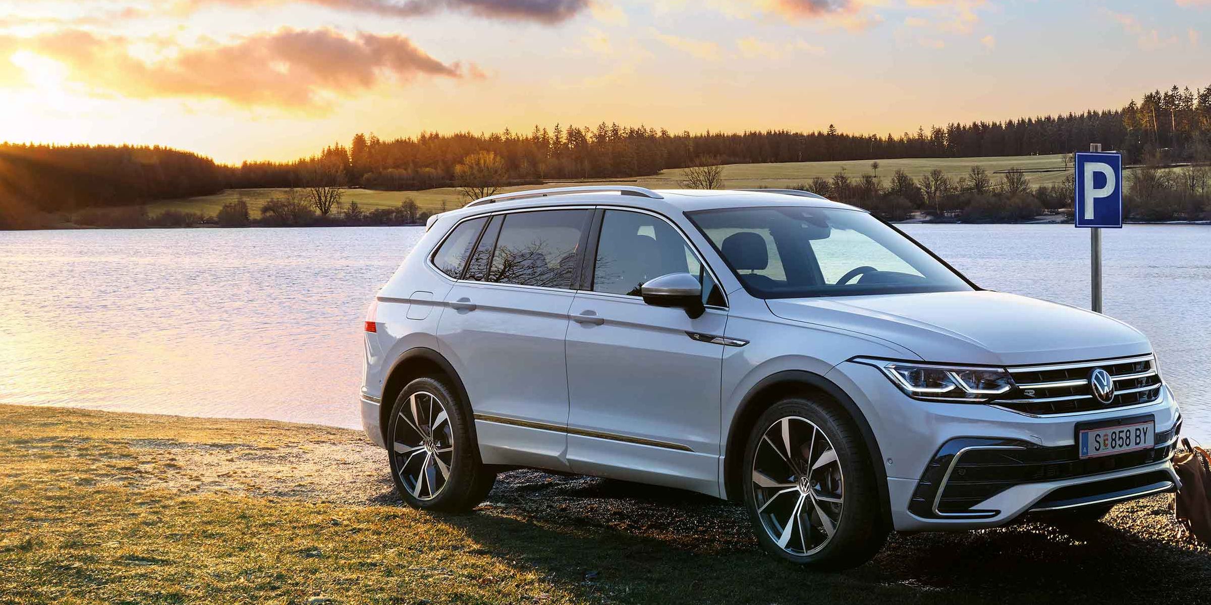 Mann steht neben einem weißen VW Tiguan Allspace, der am Seeufer geparkt ist