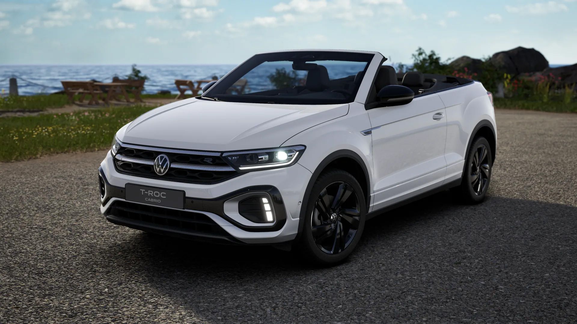T-Roc Cabriolet R-Line in Weiß mit schwarzen Leichtmetallrädern und schwarzen Außenspiegeln vor Küstenkulisse.