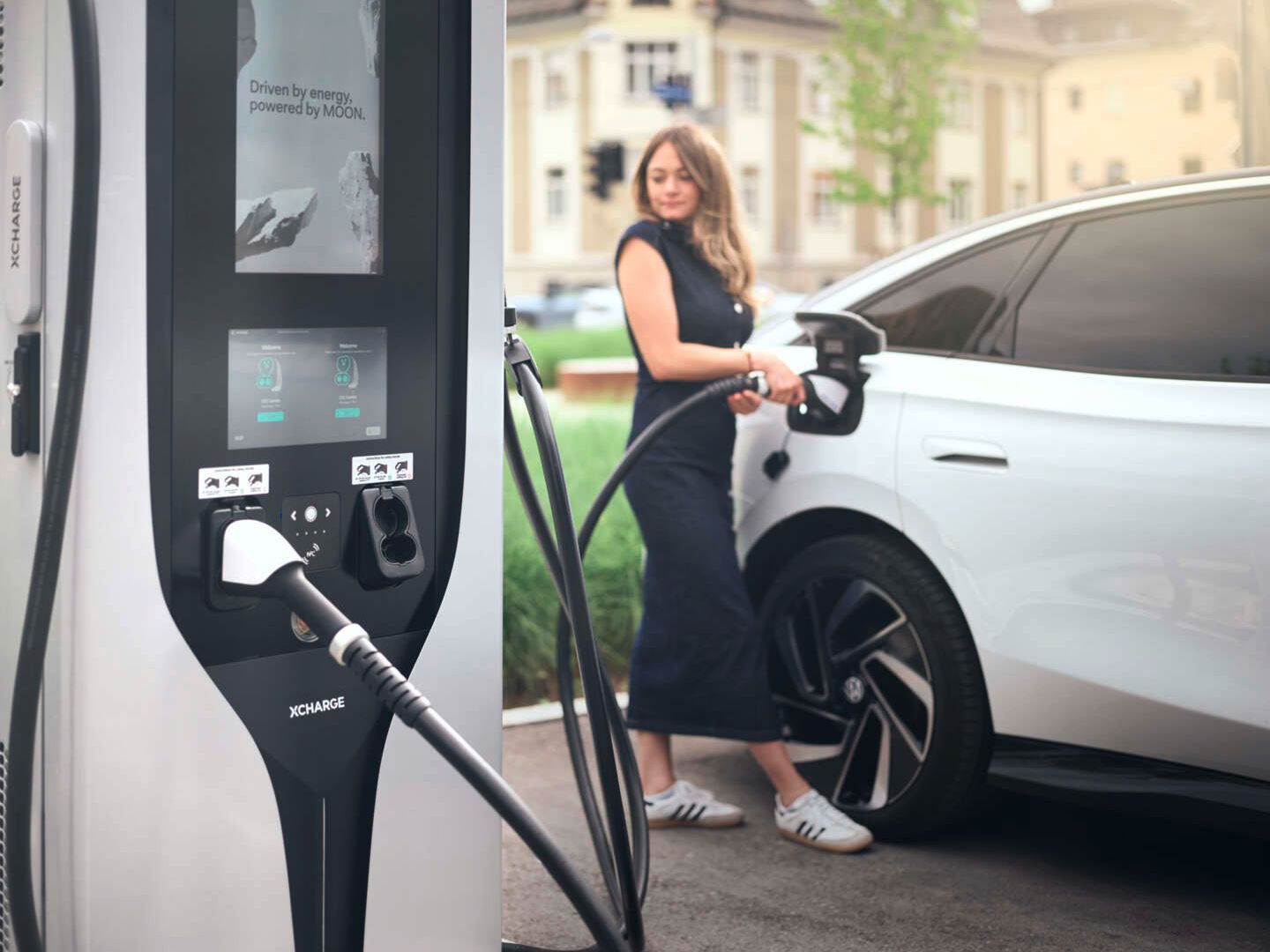 Frau lädt einen weißen VW ID.7 per MOON Ladestation mit Strom.