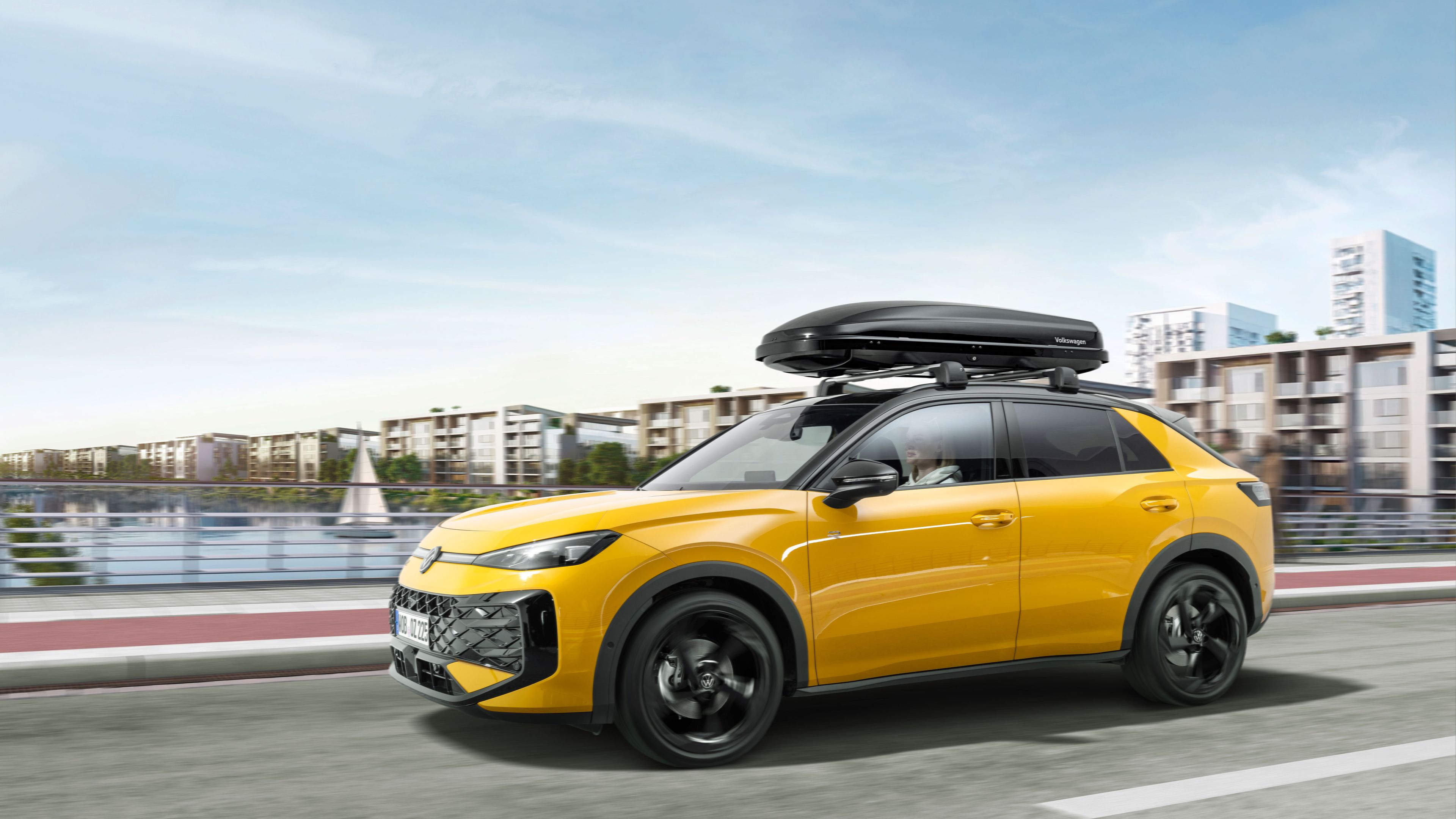 Ein gelber T-Roc mit Dachbox in Fahrt über eine Brücke.