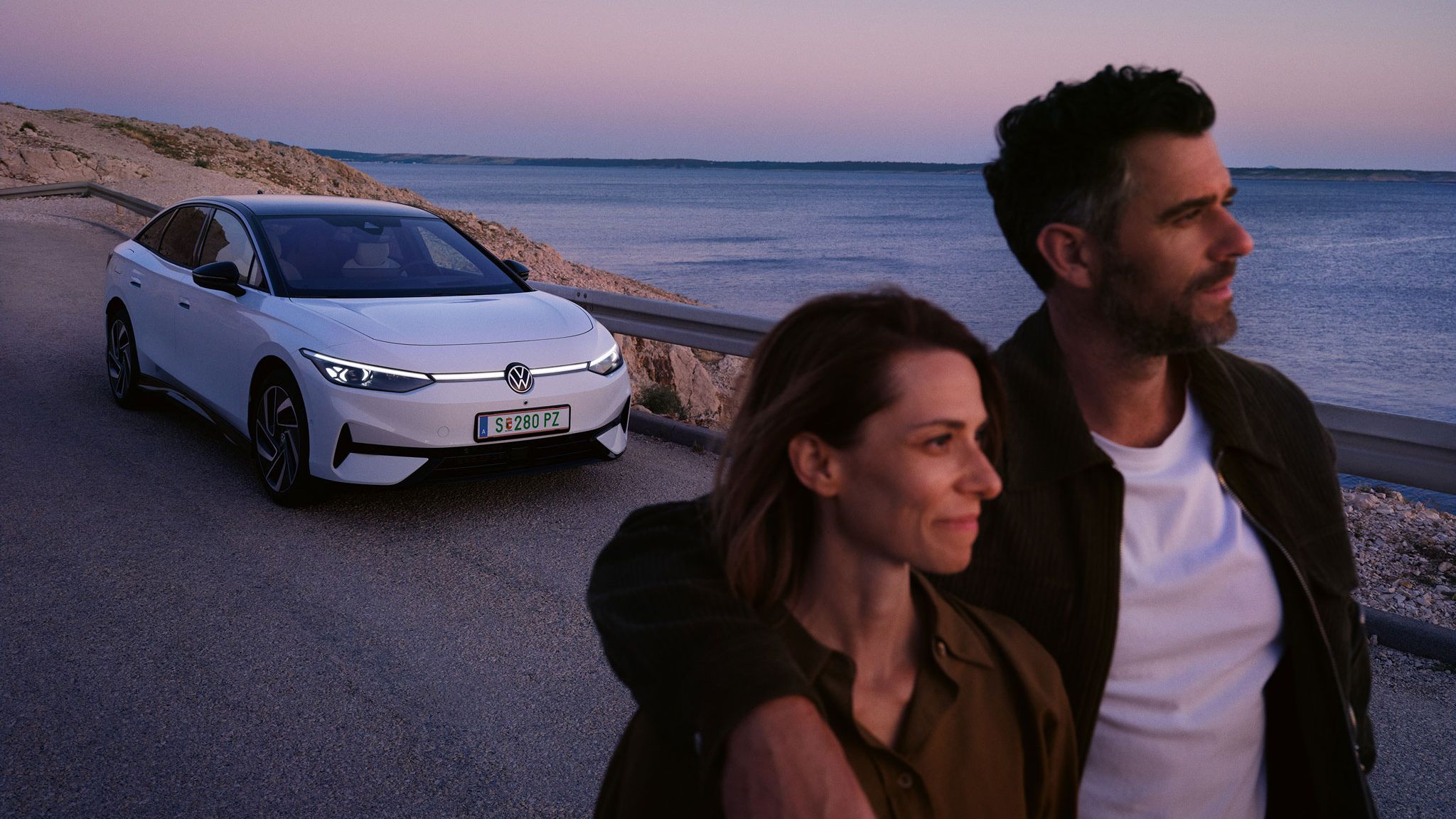 Ein Pärchen läuft am Meer entlang, im Hintergrund parkt ein ID.7 