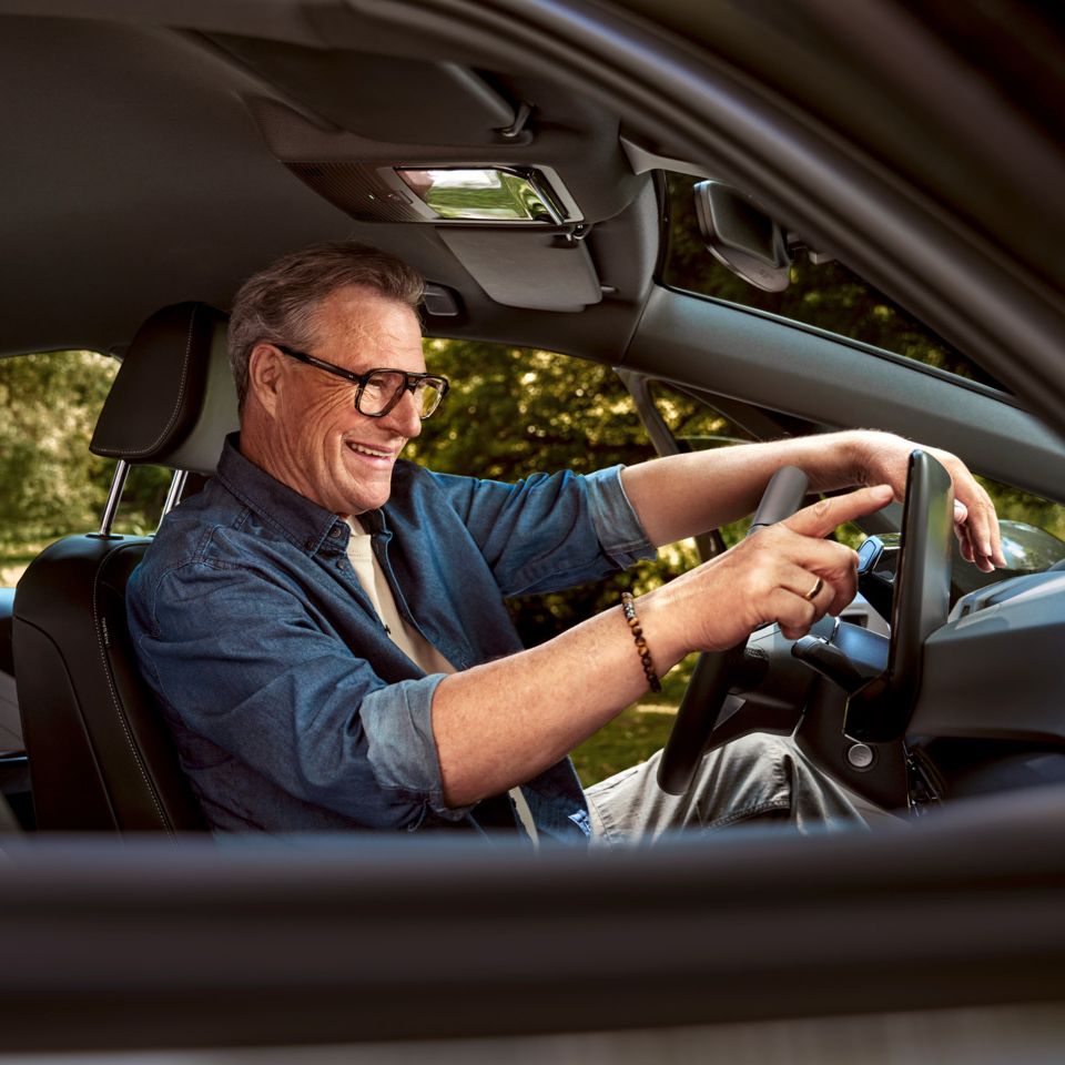 Ein Mann sitzt auf dem Fahrersitz seines geparkten ID.3 und tippt auf das HMI