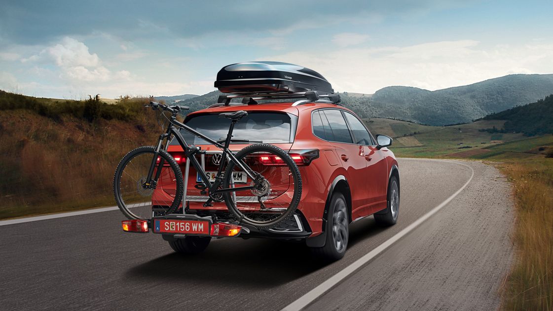 Ein roter Volkswagen Tiguan mit Fahrradheckträger und einer Dachbox fährt auf einer Landstraße