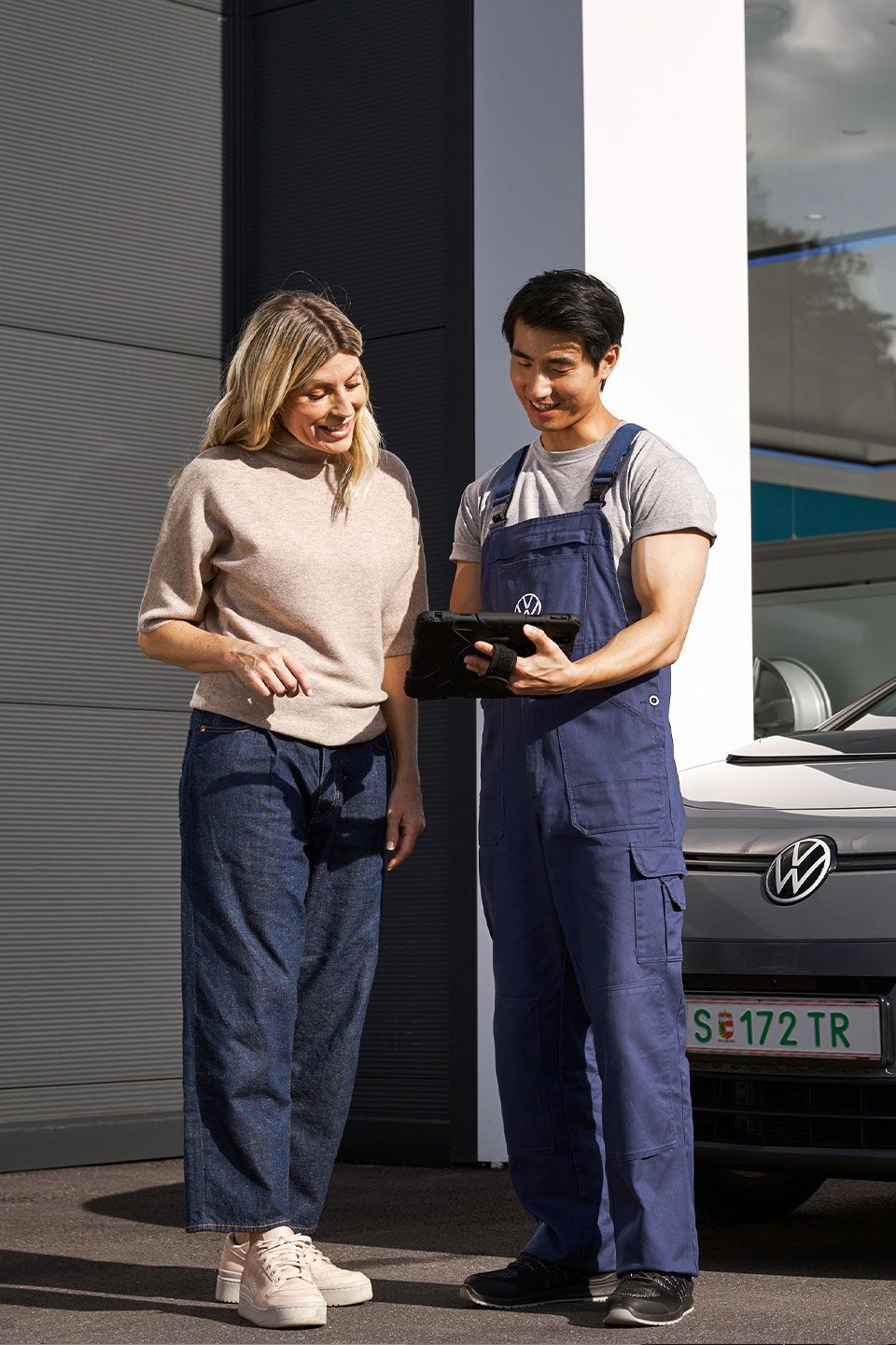 Ein Volkswagen Techniker und eine Kundin stehen vor einem grauen Volkswagen ID.3
