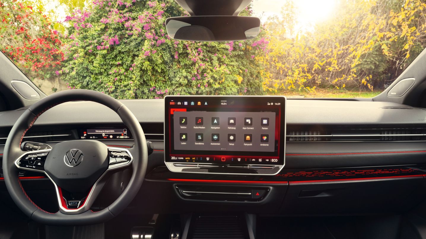 Cockpit eines VW ID.7 GTX mit Multifunktionslenkrad und Infotainmentsystem mit roten Akzenten.