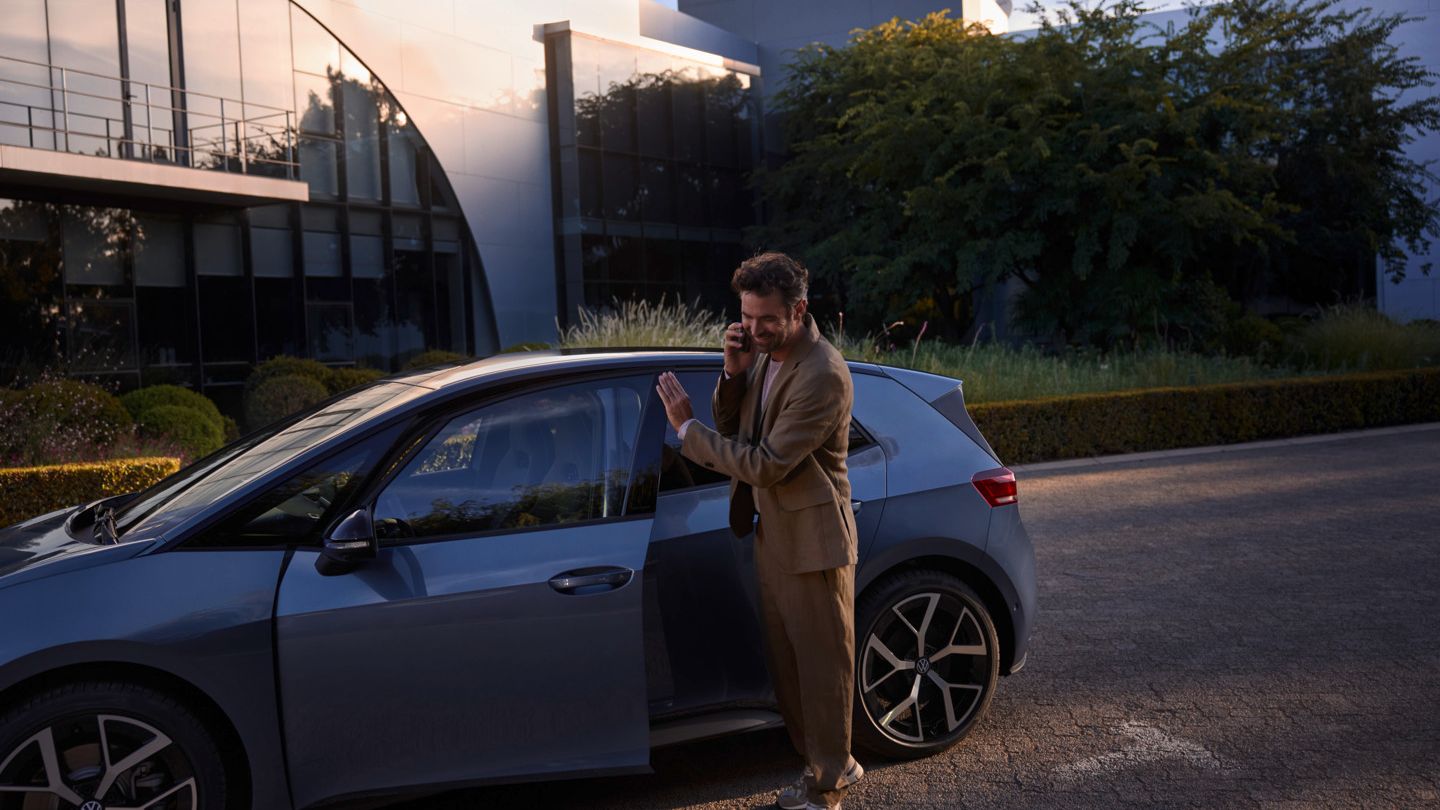 Ein Mann steht vor einem blauen VW ID.3 Neo und telefoniert per Smartphone