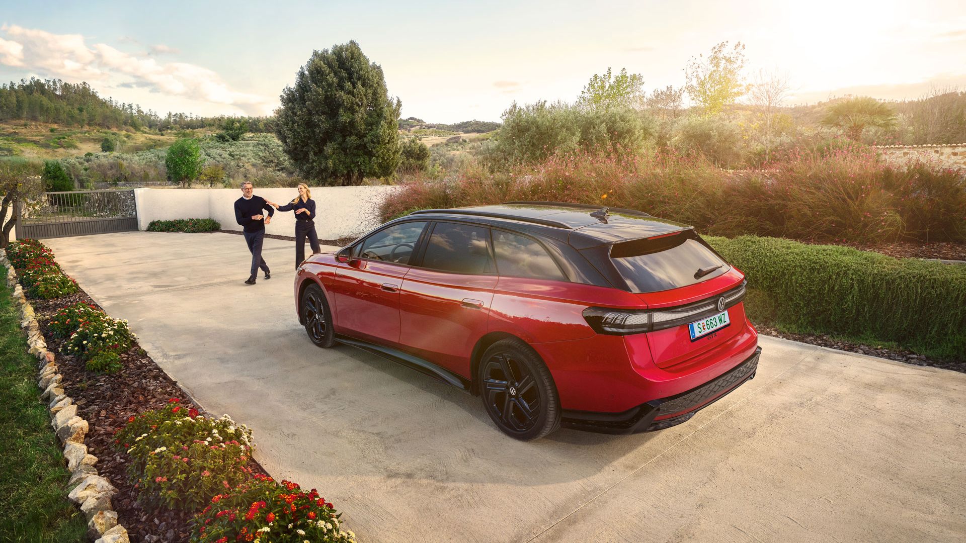 Ein roter VW ID.7 GTX Tourer parkt in einer langen Auffahrt, ein Mann und eine Frau wollen einsteigen.
