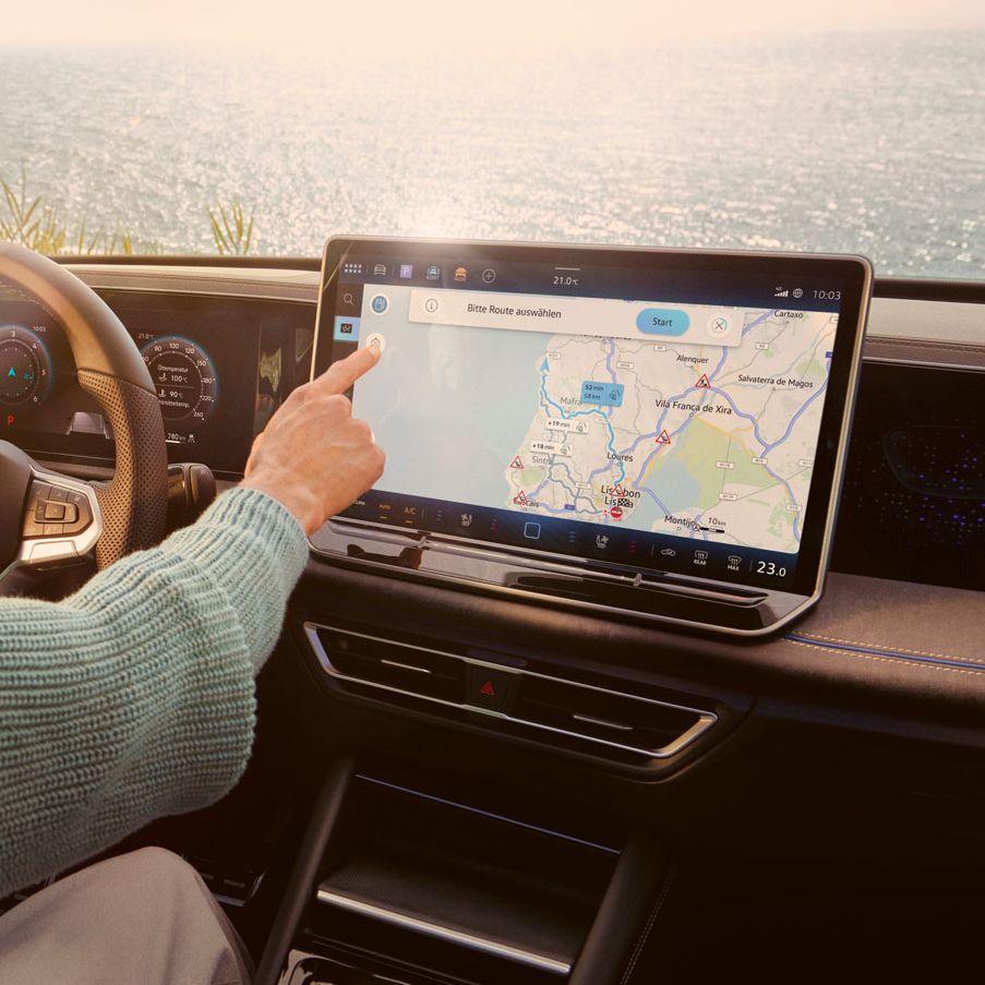 Frau sitzt auf dem Fahrersitz eines geparkten VW Tiguan und bedient den Touchscreen des Infotainment-Systems mit Kartenansicht.