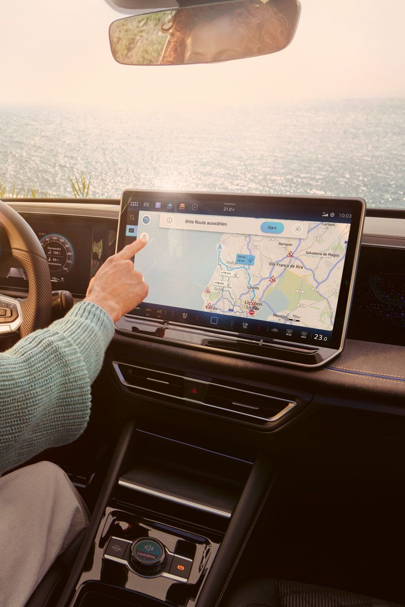 Frau sitzt auf dem Fahrersitz eines geparkten VW Tiguan und bedient den Touchscreen des Infotainment-Systems mit Kartenansicht.