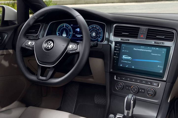 Das Bild zeigt das Innere eines VW e-Golf, besonders das Armaturenbrett. Es sind das Lenkrad, die Instrumententafel und ein großer Touchscreen-Bildschirm sichtbar.
