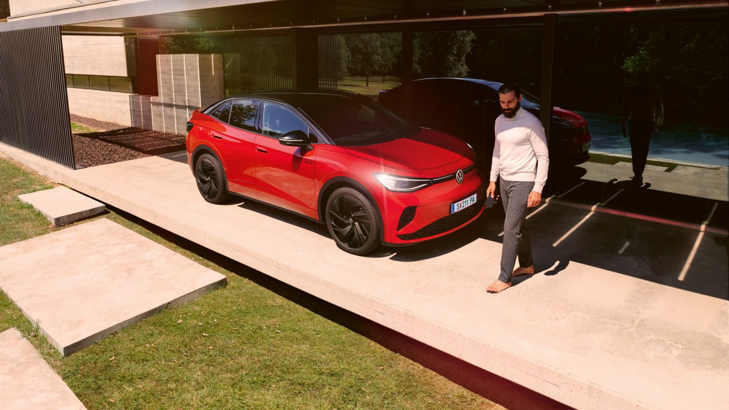 Ein roter VW ID.5 GTX steht seitlich vor einem modernen Bungalow, ein Mann geht daran vorbei.