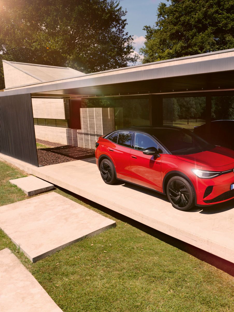 Ein roter VW ID.5 GTX steht seitlich vor einem modernen Bungalow, ein Mann geht daran vorbei.