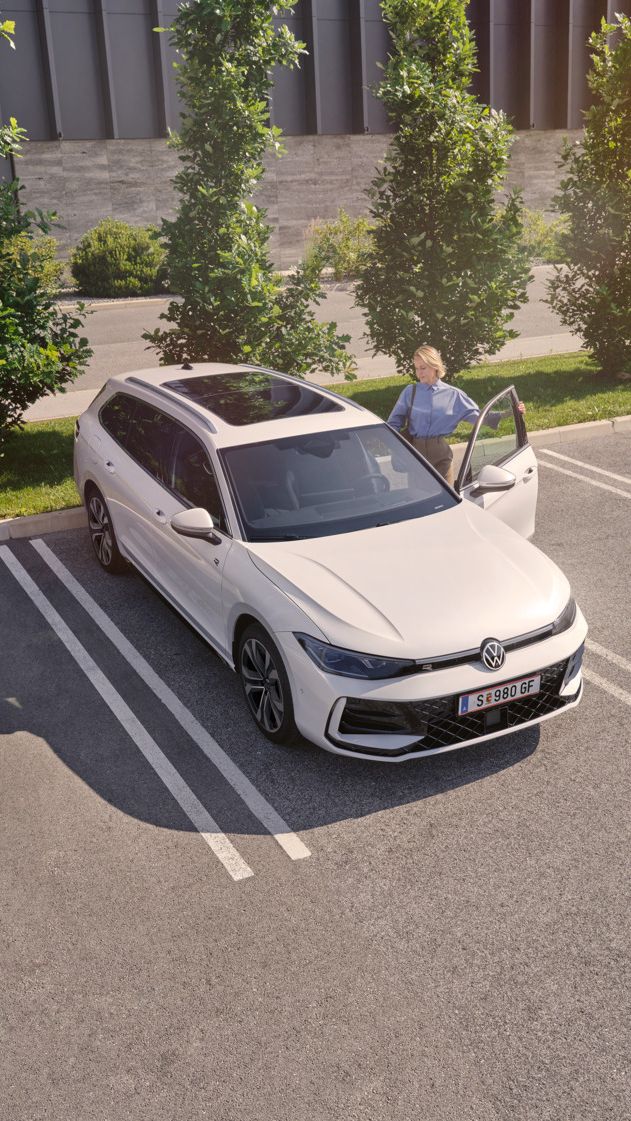 Weißer VW Passat parkt vor einem modernen Bürogebäude. Eine Frau steigt ein.