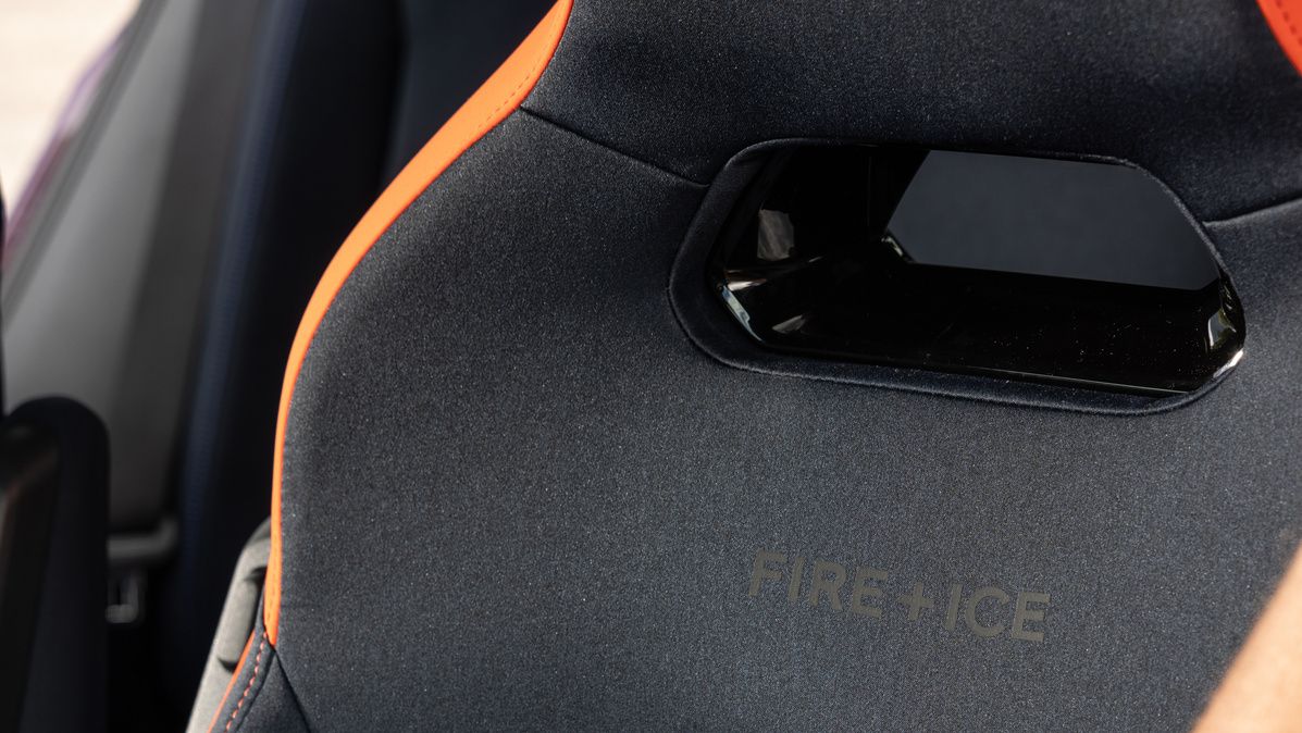 Nahaufnahme eines Autositzes, dessen Bezug teilweise geöffnet ist. Eine Hand hält die offene Seite, und zeigt ein gesticktes Emblem auf dem darunterliegenden Stoff.