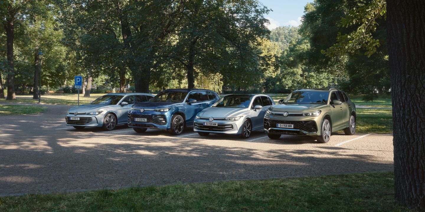 Vier VW Plug-In-Hybrid-Modelle stehen nebeneinander auf einem Parkplatz in einem Park.