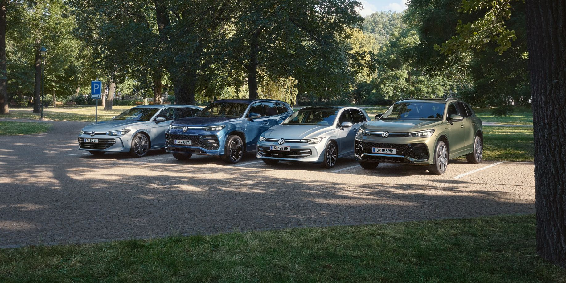 Vier VW Plug-In-Hybrid-Modelle stehen nebeneinander auf einem Parkplatz in einem Park.