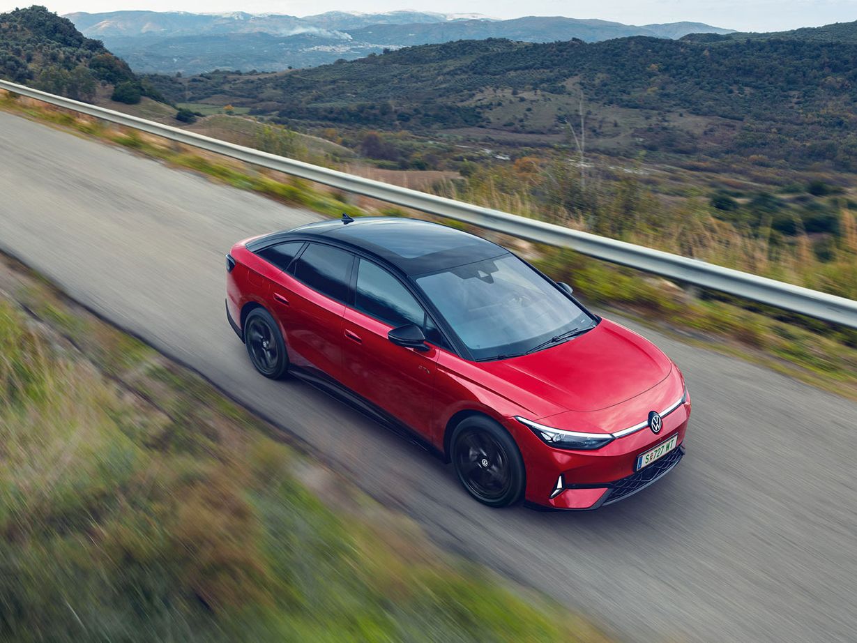 Blick auf die aerodynamisch gestaltete Front eines roten VW ID.7 GTX, der durch eine Berglandschaft fährt.