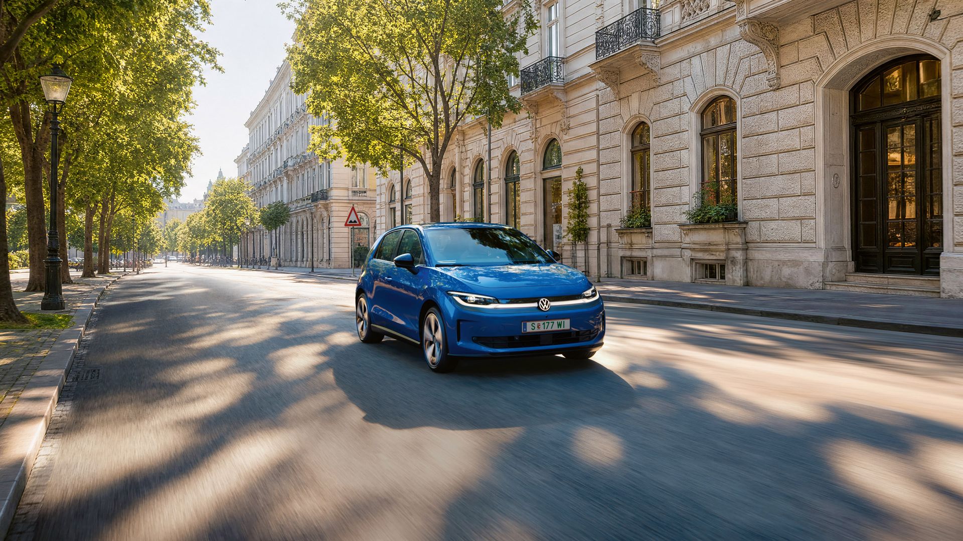 Ein blauer VW ID. Polo fährt auf einer breiten Straße im Schatten einer Allee.