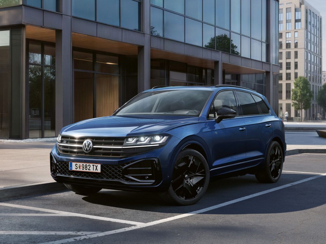 Ein blauer VW Touareg Final Edition steht vor einem Bürogebäude mit Glasfassade - Ansicht von schräg vorne.