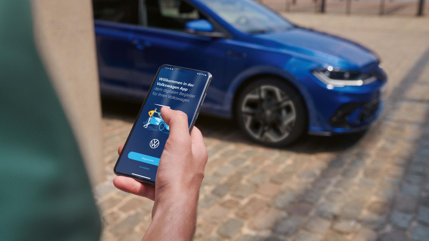 Eine Person hält ein Smartphone in der Hand mit der Volkswagen App, im Hintergrund steht ein blauer VW Polo R-Line.