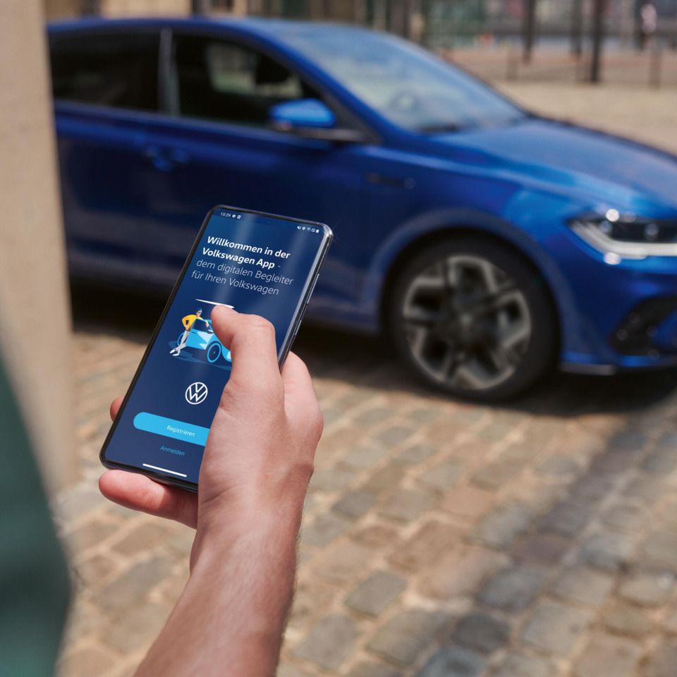 Eine Person hält ein Smartphone in der Hand mit der Volkswagen App, im Hintergrund steht ein blauer VW Polo R-Line.