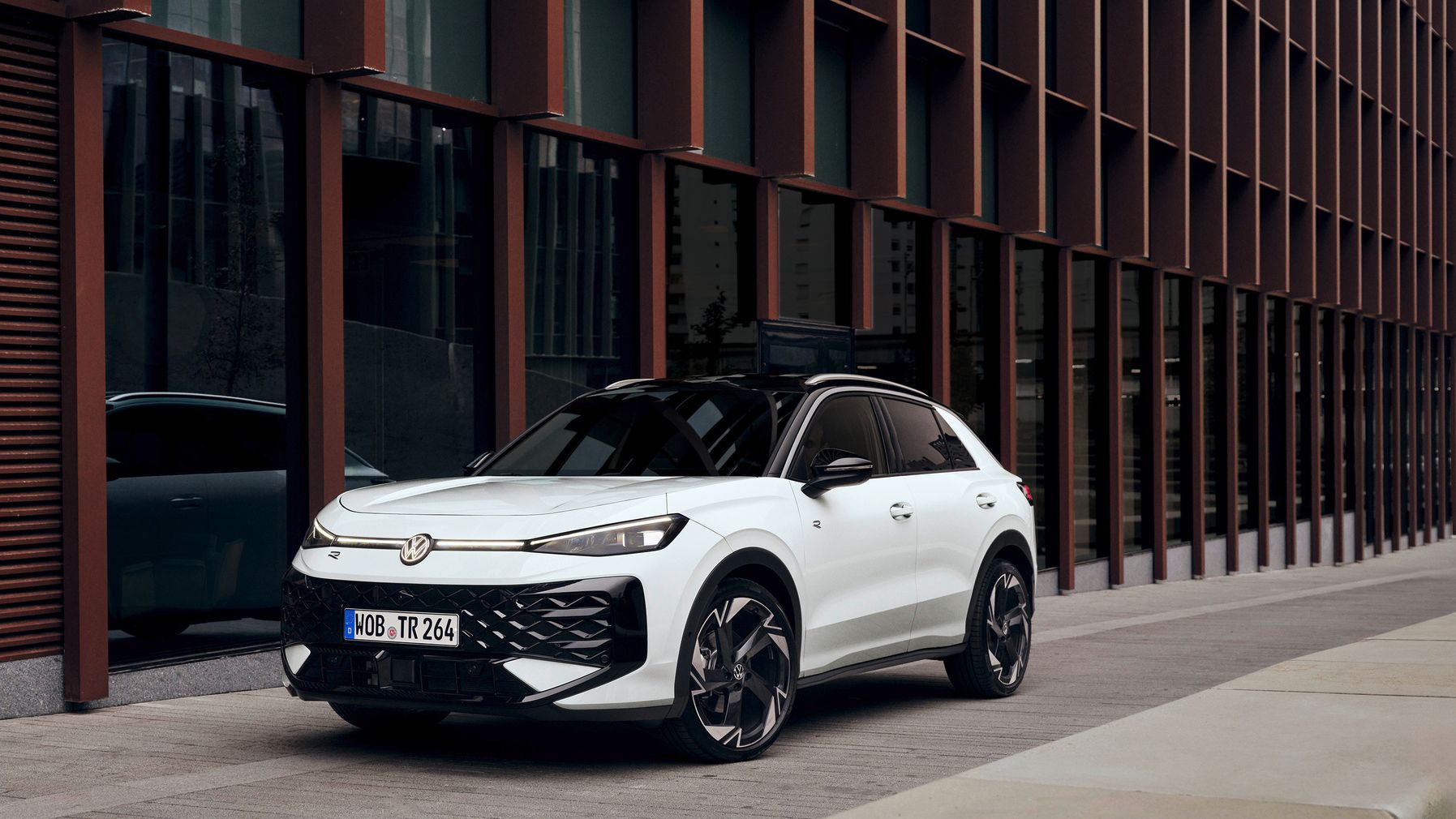 Ein weißer Volkswagen ID.5 GTX steht vor einem modernen Gebäude mit großen Glasfenstern. Der Wagen hat schwarze Akzente und sportliche Felgen.