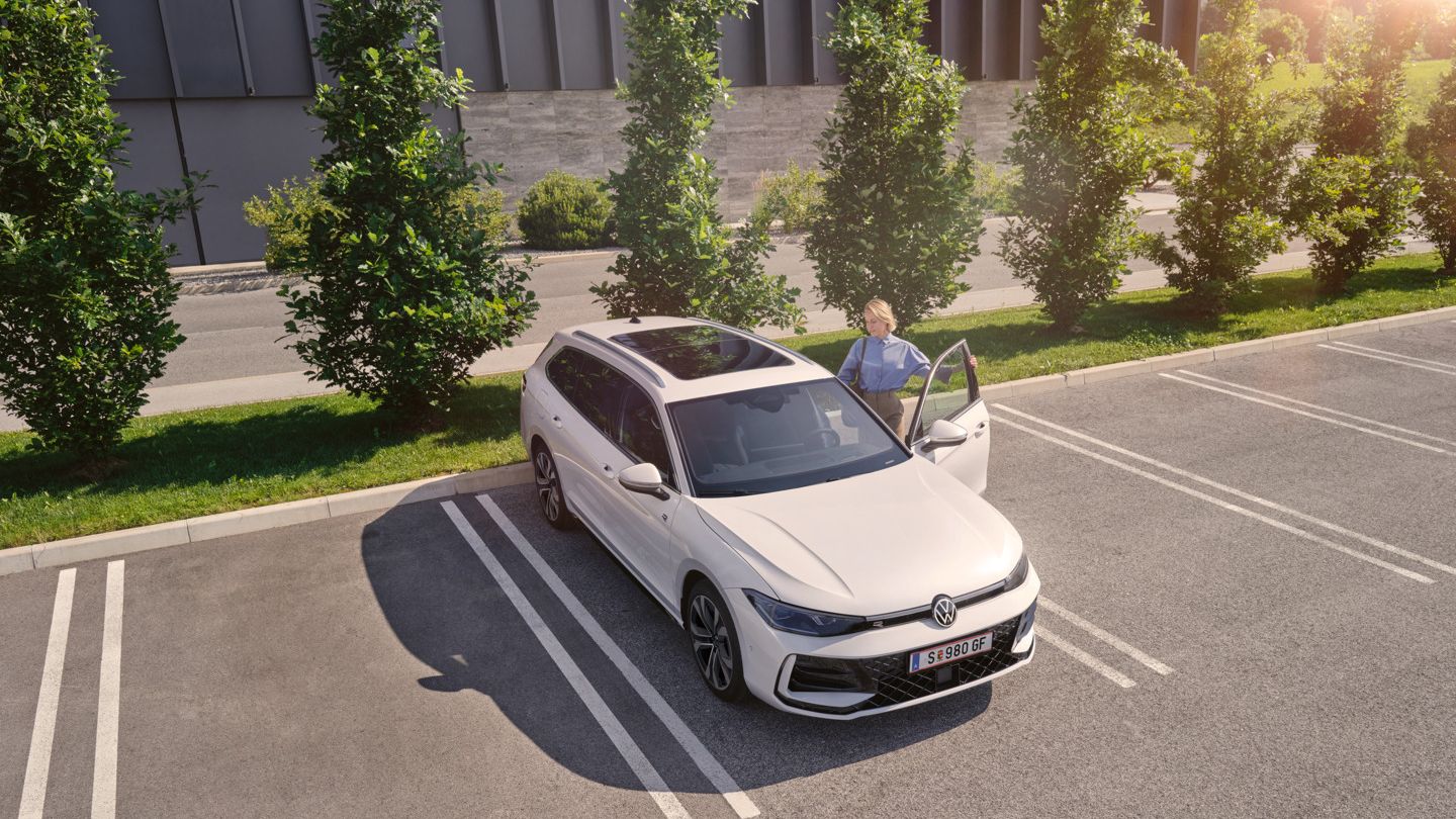 Weißer VW Passat parkt vor einem modernen Bürogebäude. Eine Frau steigt ein.