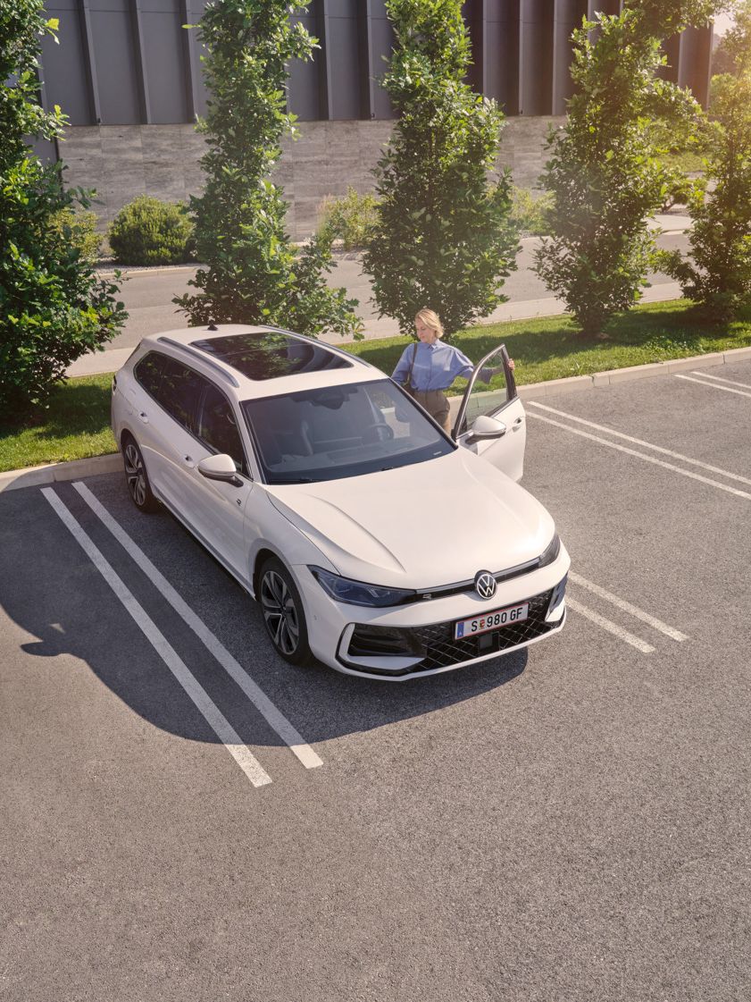 Weißer VW Passat parkt vor einem modernen Bürogebäude. Eine Frau steigt ein.