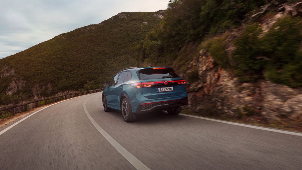 Roter VW Tiguan in Heckansicht fährt durch eine bergige Landschaft.