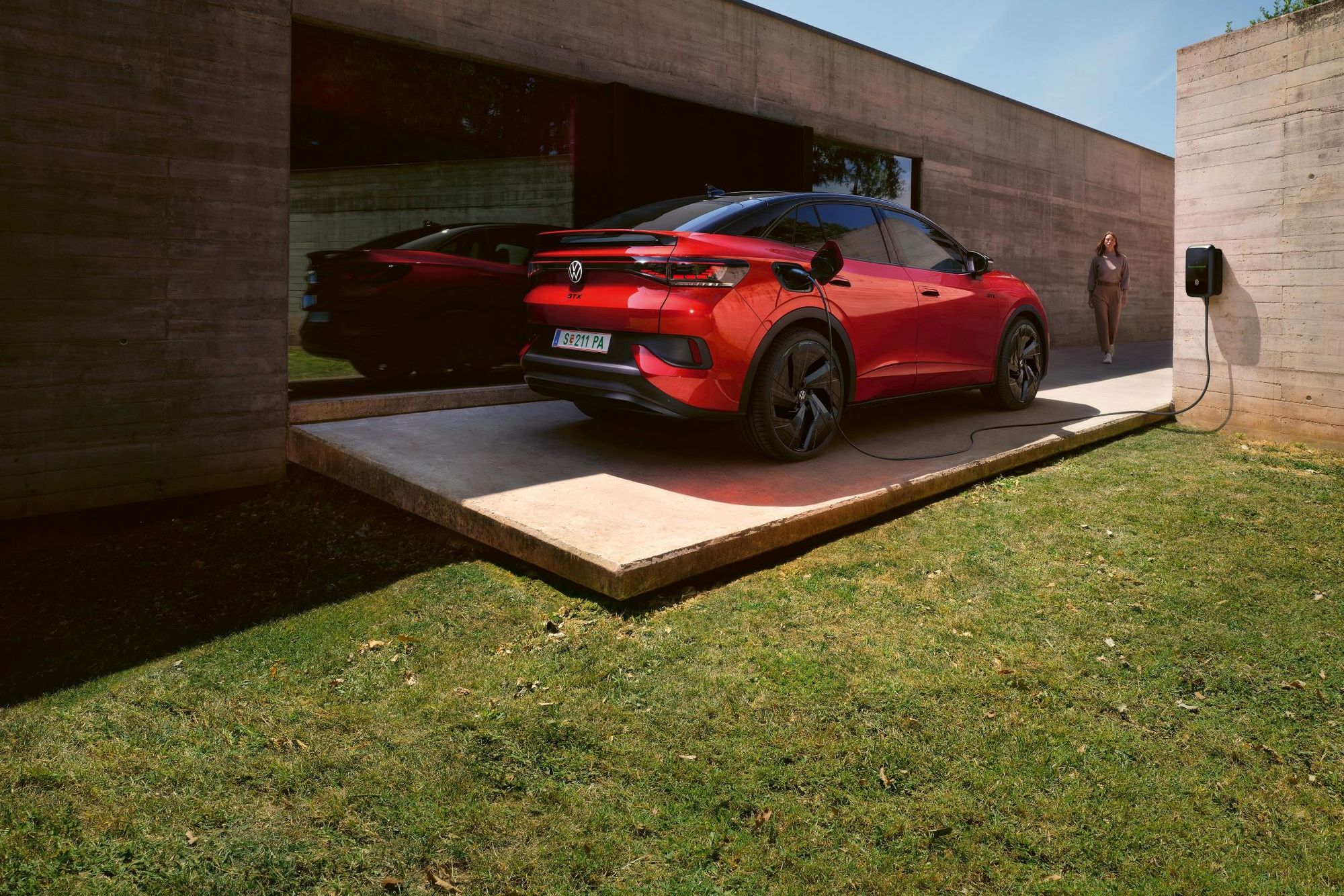 Ein roter VW ID.5 GTX lädt an einer Wallbox neben einem Bungalow mit großer Glasfront.