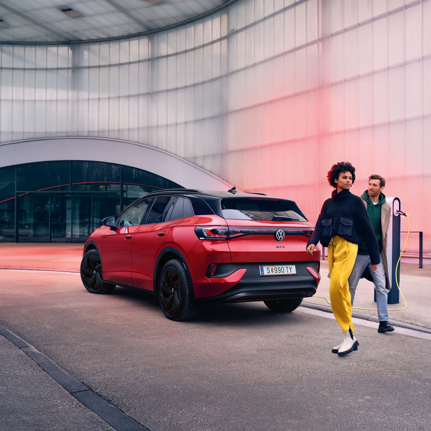 Heckansicht eines roten VW ID.4 GTX, davor überqueren zwei Personen die Straße