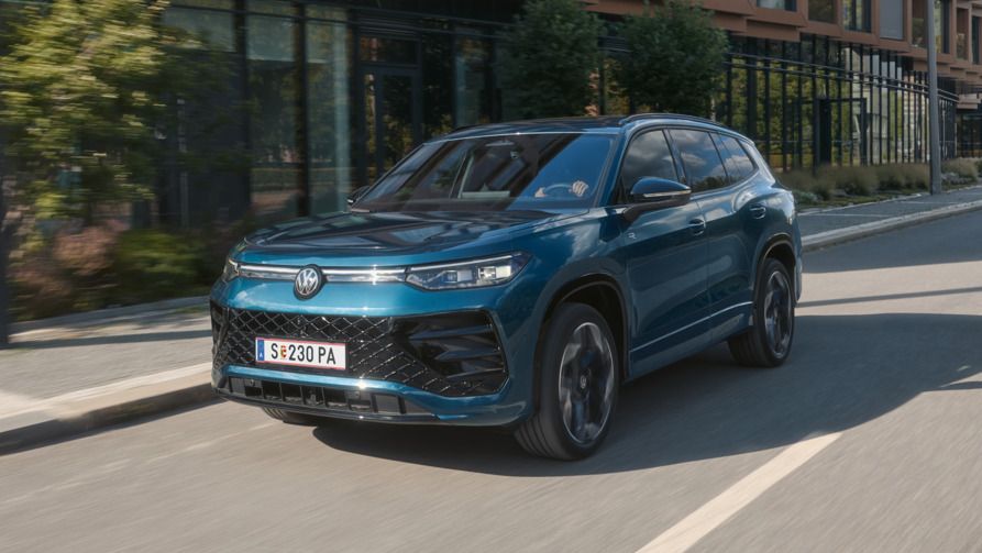 Ein VW Tayron R-Line Plug-In-Hybrid fährt vor modernen Gebäuden in einer urbanen Umgebung.