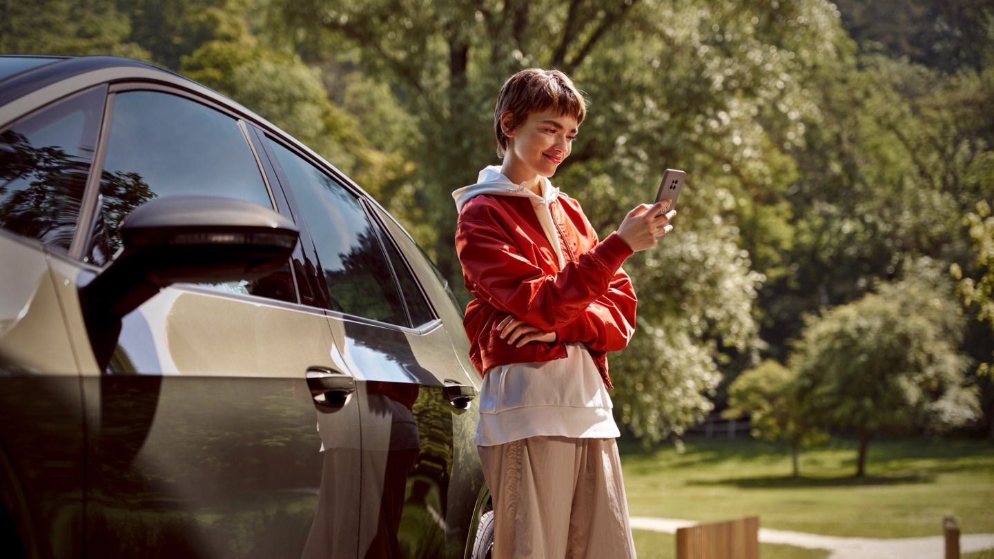 Eine Frau mit einem Smartphone steht neben ihrem ID.3
