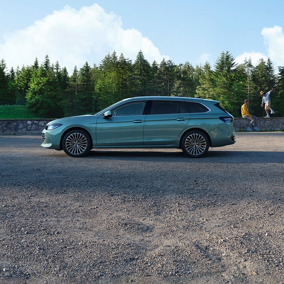 Seitenansicht eines grünen VW Passat Elegance vor einem Wald, im Hintergrund sieht man einen Mann und einen Jungen.